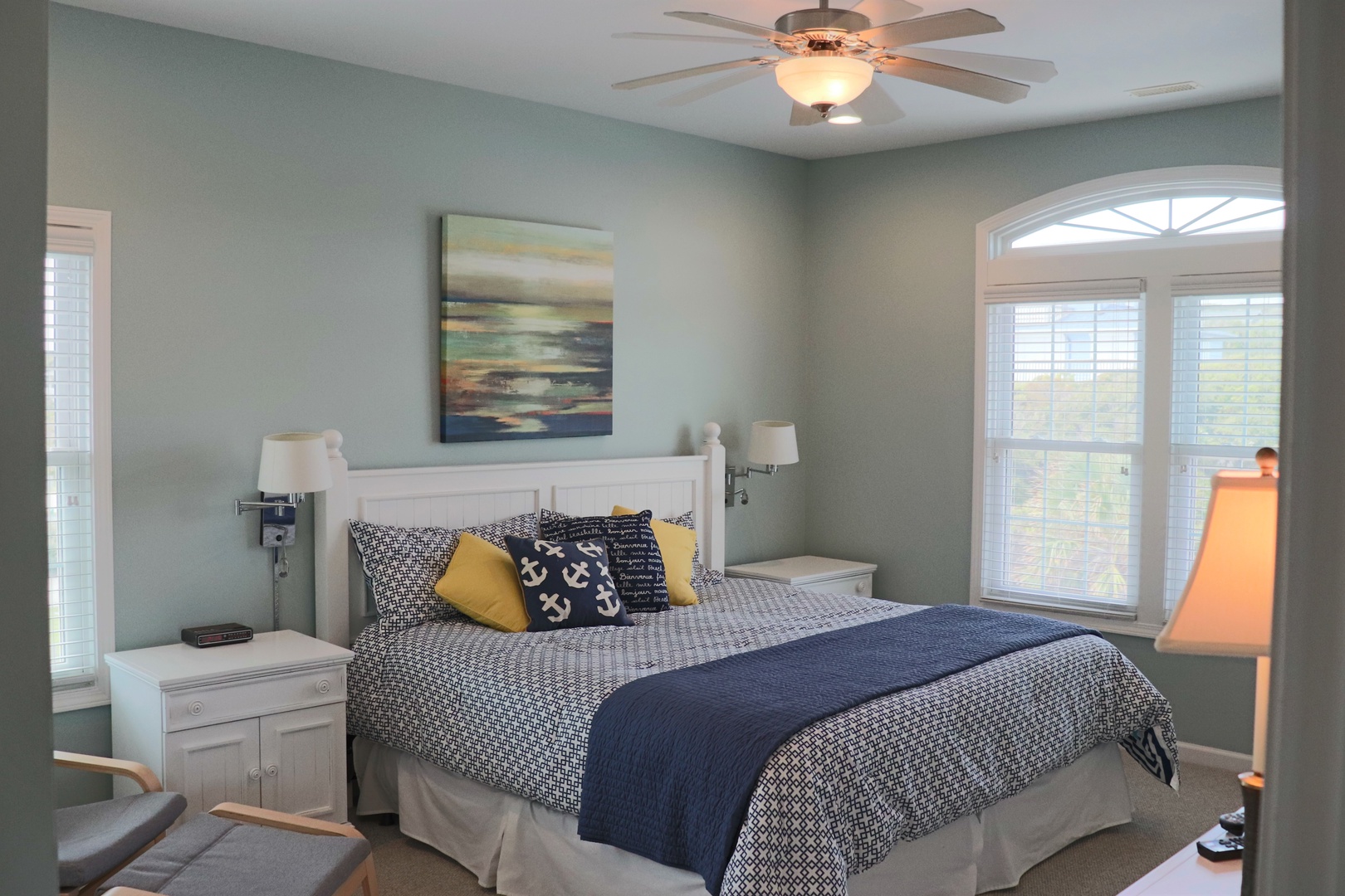 Sink into comfort in your serene bedroom, featuring crisp white furnishings, coastal artwork, and natural light streaming through windows.