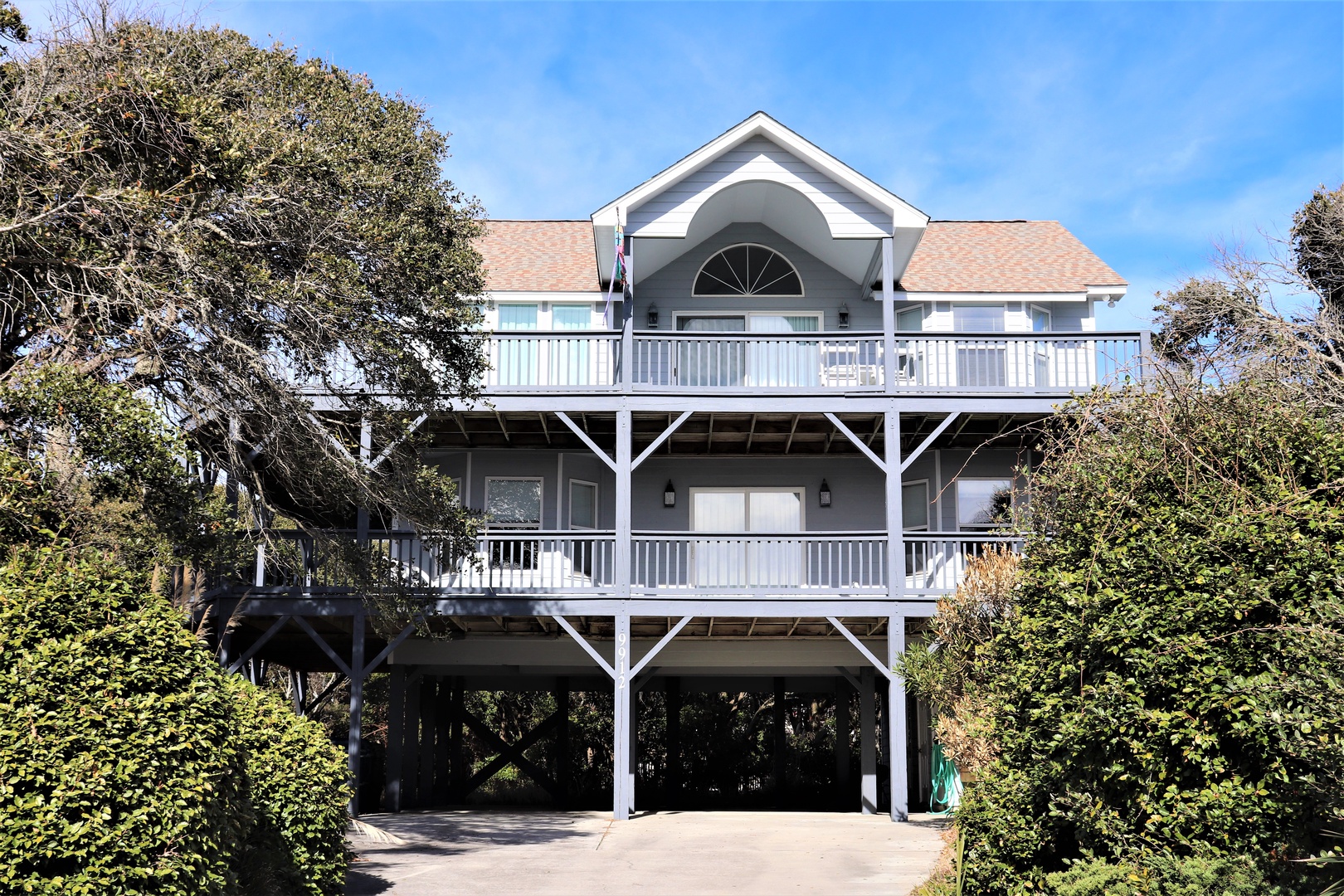 Charming coastal home with two-story wraparound decks nestled among mature trees, offering elevated seaside living with covered parking below.