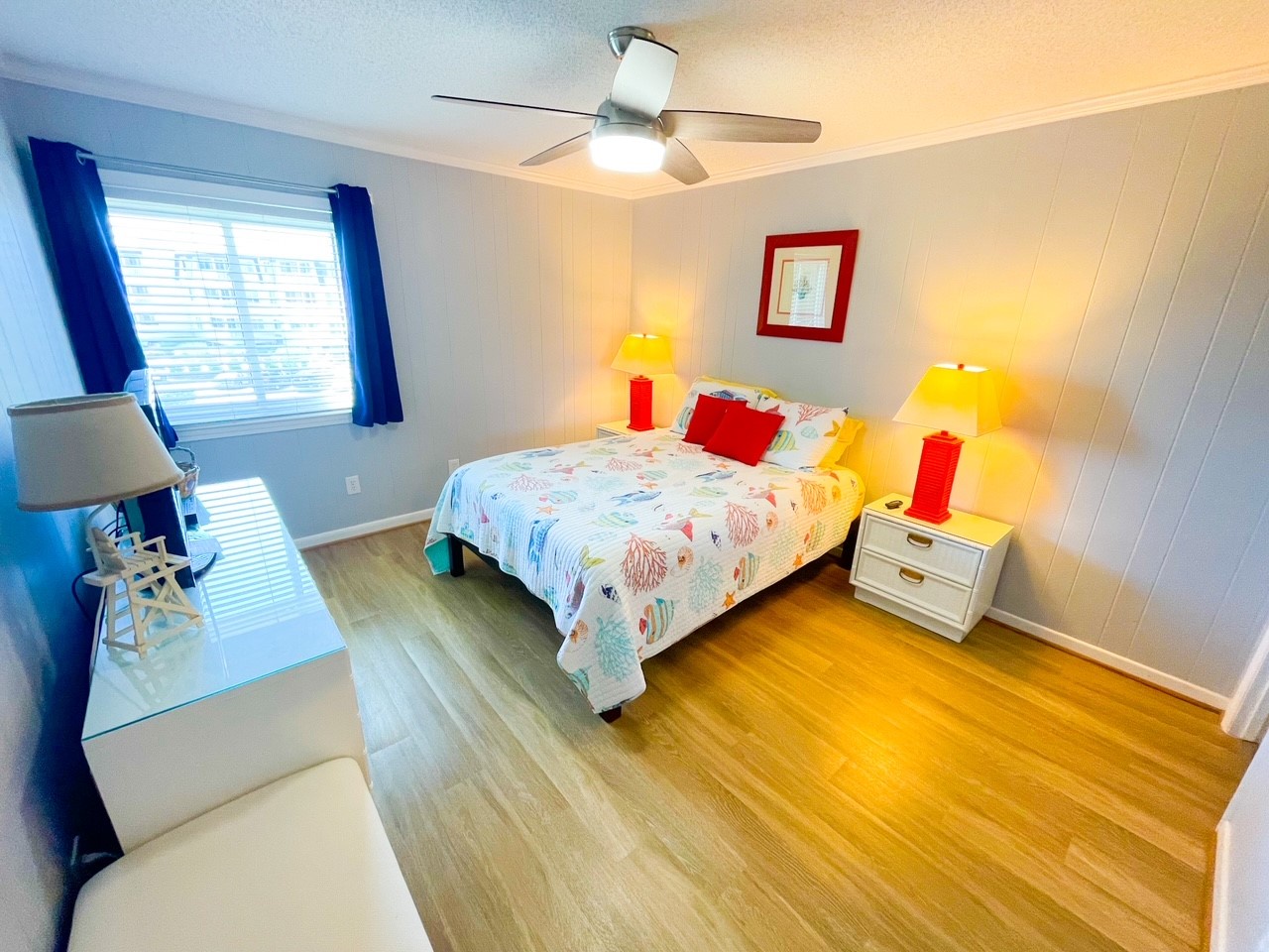 Sink into crisp coastal-themed bedding as warm lamplight creates your perfect bedtime glow in this cheerful bedroom.