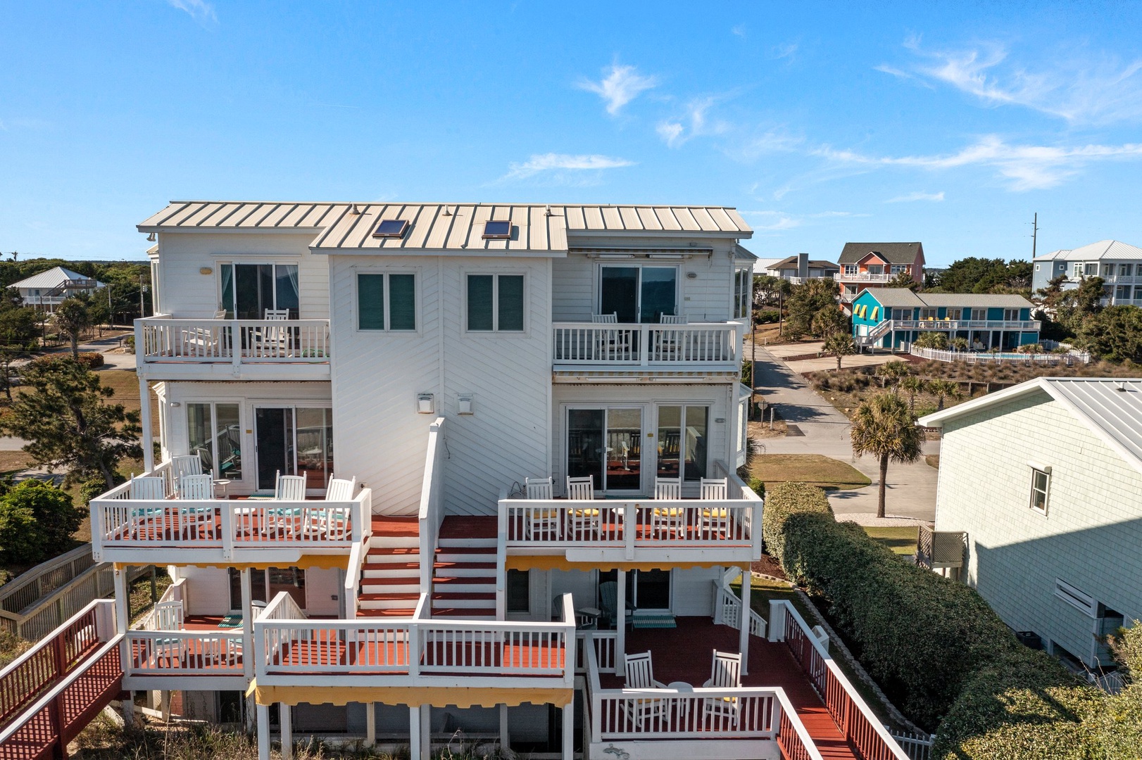 This multi-story beach house features expansive decks and balconies, nestled among coastal homes in a peaceful neighborhood setting.
