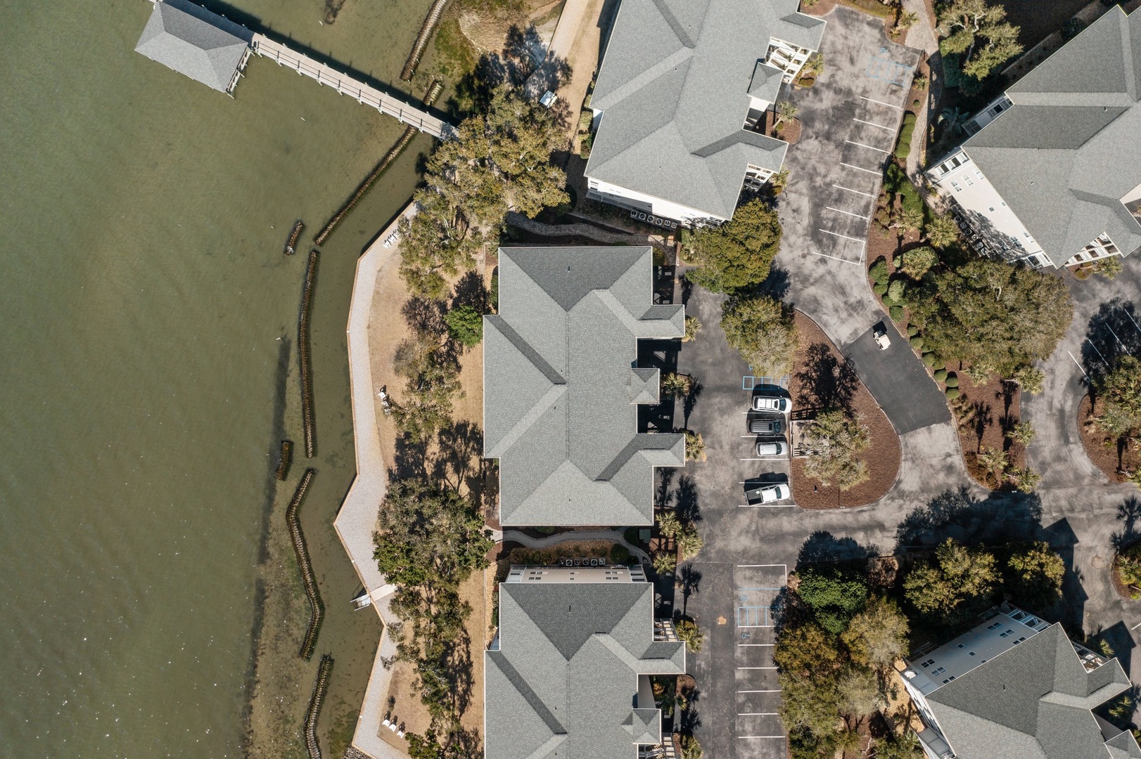 Aerial view of waterfront property buildings with parking areas and mature landscaping near calm waters.