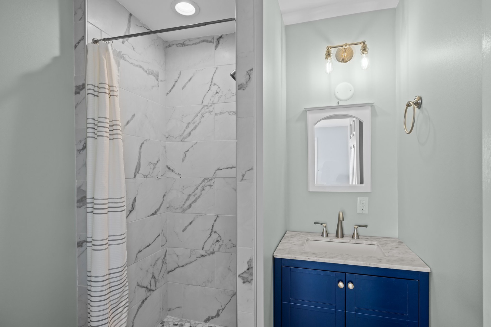 Step into your serene bathroom featuring elegant marble-look shower tiles and stylish navy vanity with modern gold fixtures.