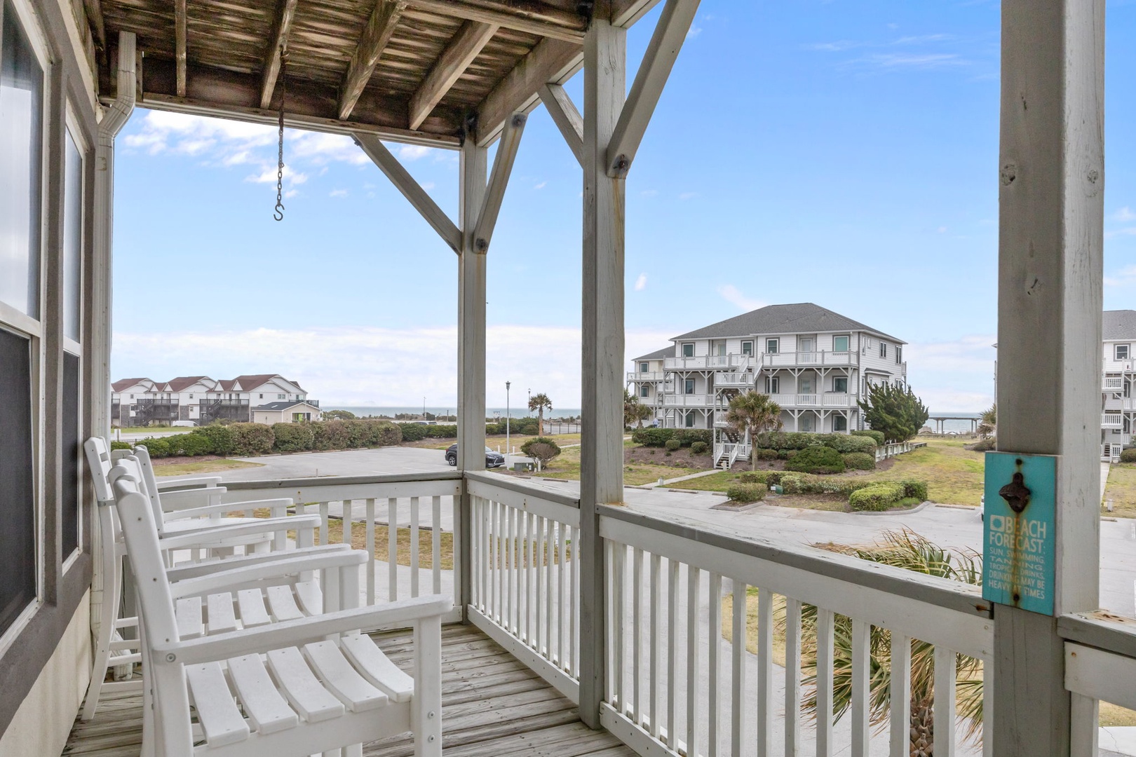 Relax on your covered porch with white rocking chairs, taking in coastal neighborhood views under clear blue skies.