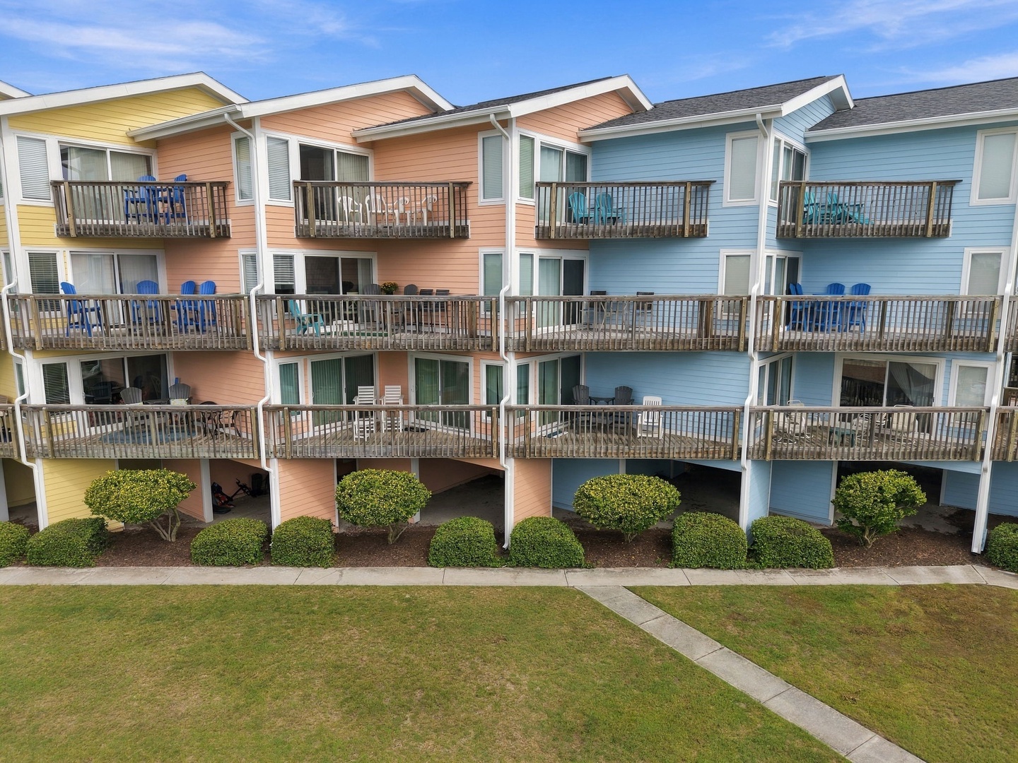 A cheerful row of colorful beachside condos with private balconies, set against a bright coastal sky and surrounded by manicured greenery.