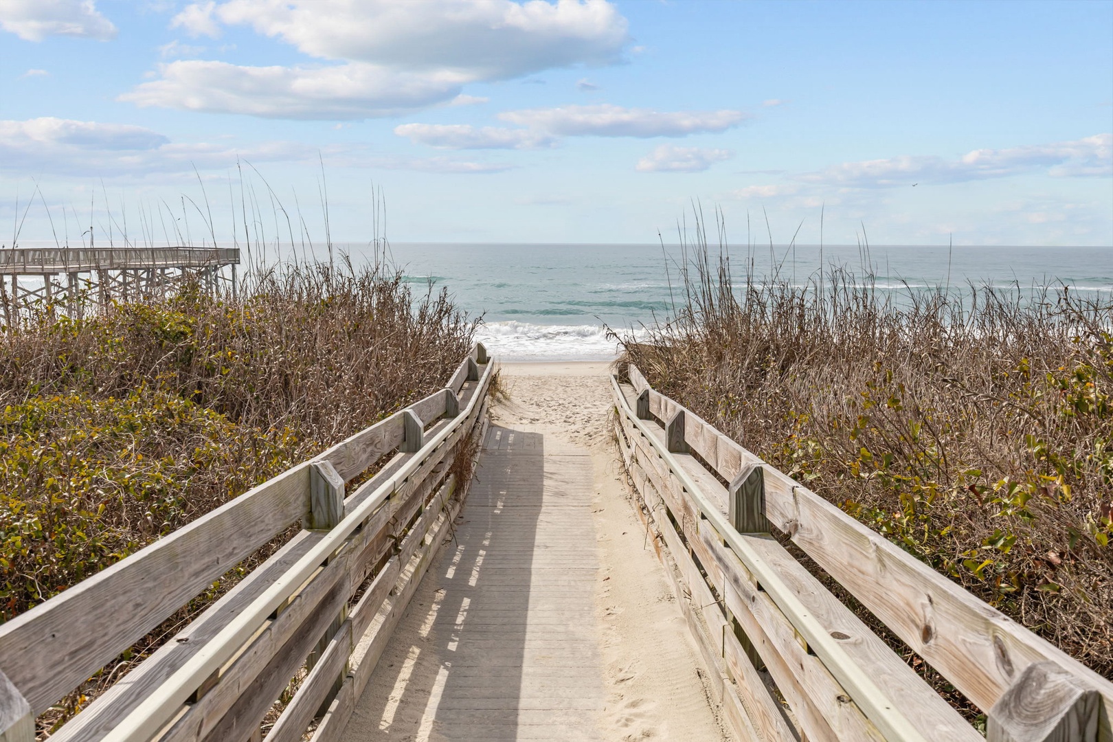Scenic wooden boardwalk leads through coastal dunes to pristine beach and ocean waves.