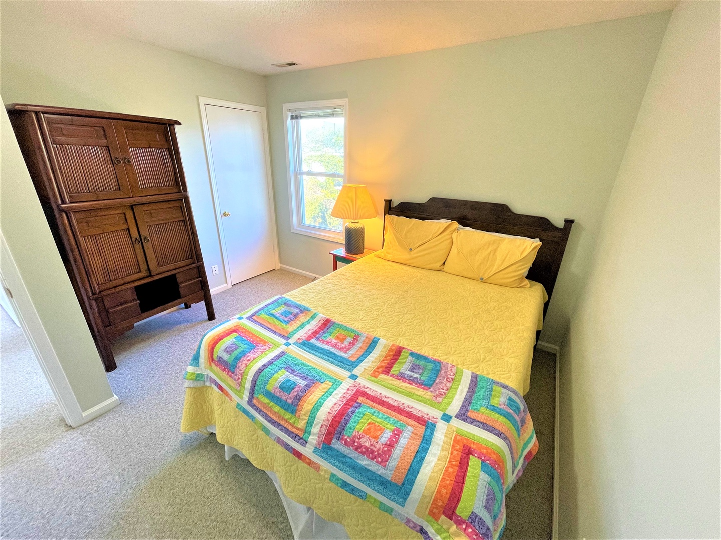 Drift off to sleep in your cozy bedroom featuring a cheerful quilt, warm lighting, and peaceful views through the windows.