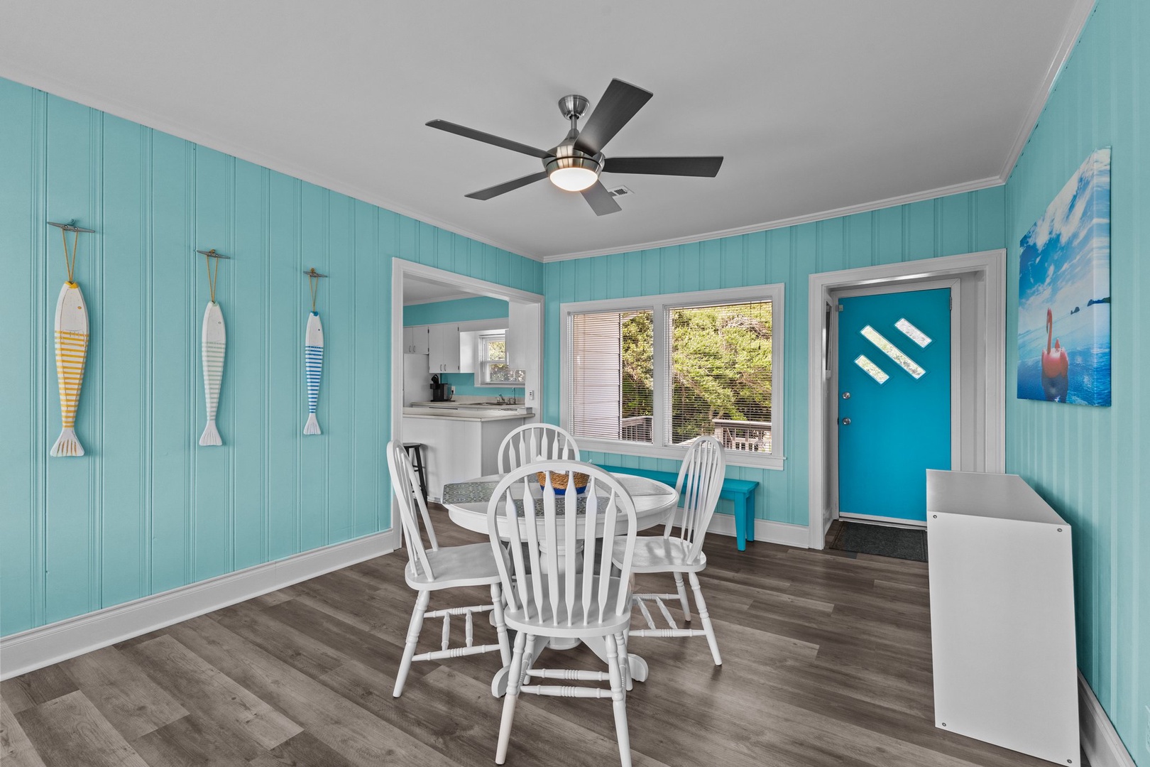 Gather around your charming dining table beneath the coastal-inspired turquoise walls and ceiling fan, perfect for enjoying meals together.