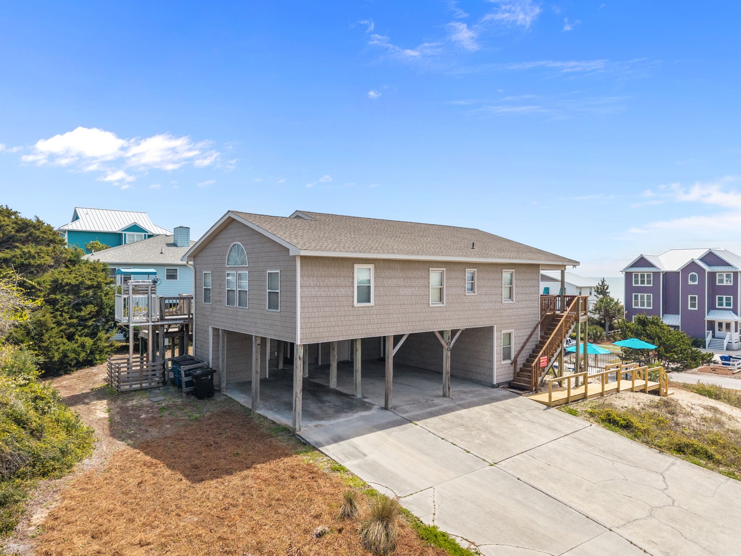 Elevated coastal vacation home with spacious ground-level parking and nearby colorful beach houses in a peaceful neighborhood setting.