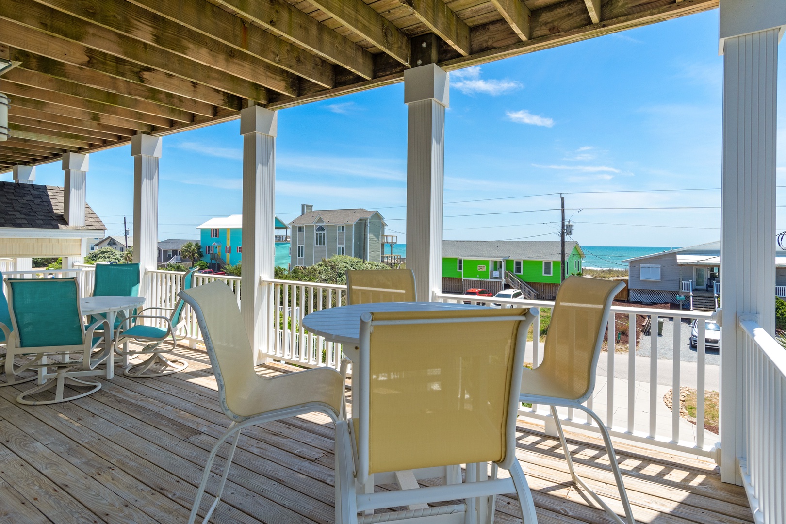 Your covered deck offers perfect ocean views with colorful beach houses dotting the coastline—ideal for morning coffee or sunset dining.