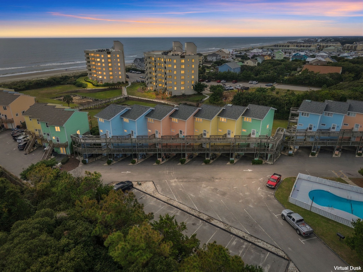 Aerial view of a colorful beachfront property featuring multi-unit townhomes with ocean access, pool facilities, and ample parking in a coastal community setting.
