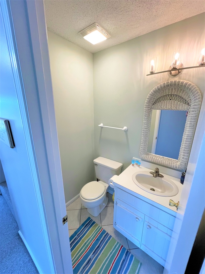Your private bathroom features a coastal-chic wicker mirror and cheerful striped rug, creating a bright, beachy vibe for your daily routines.