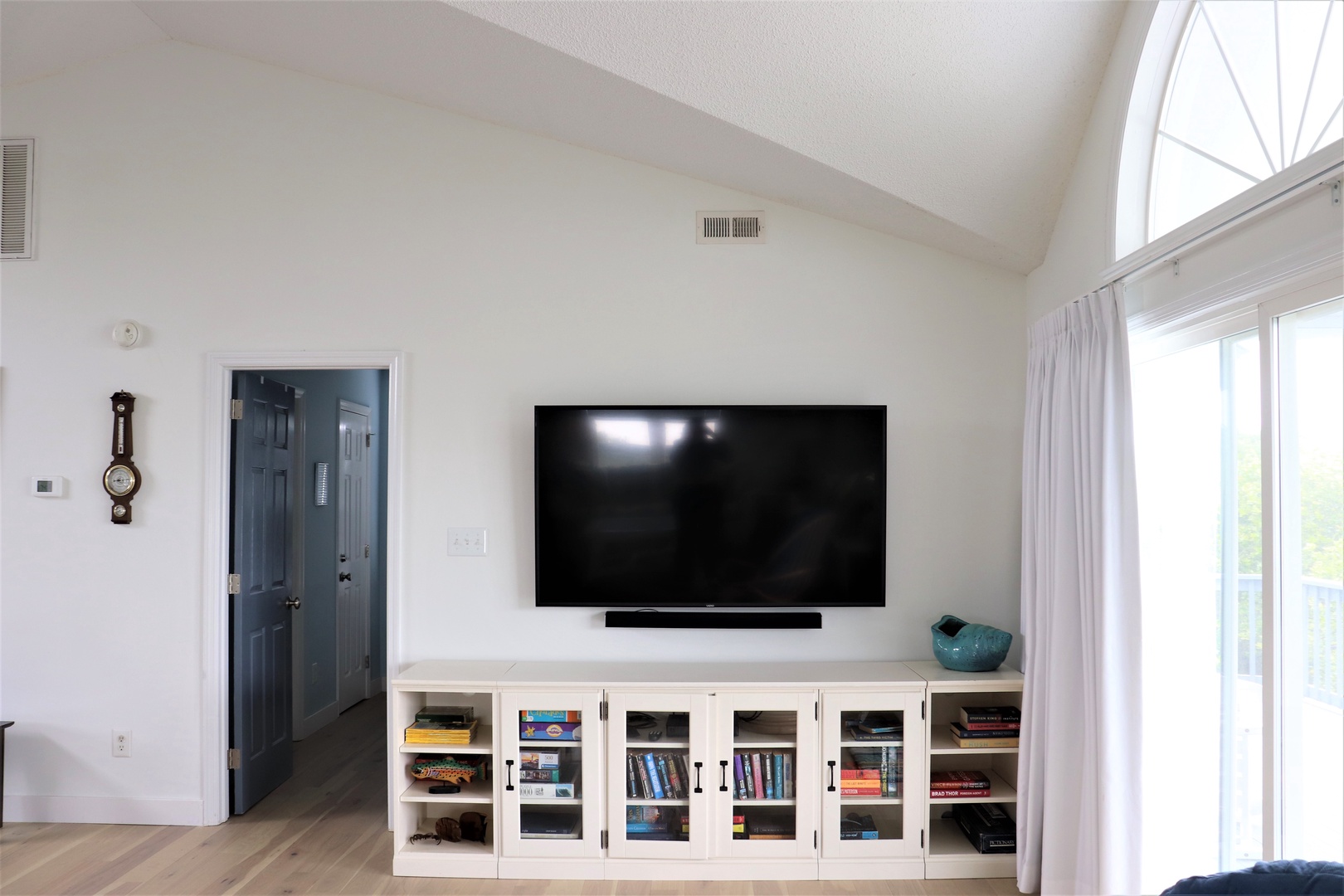 Relax in your bright living room with large windows, wall-mounted TV, and built-in storage filled with books for cozy evenings.