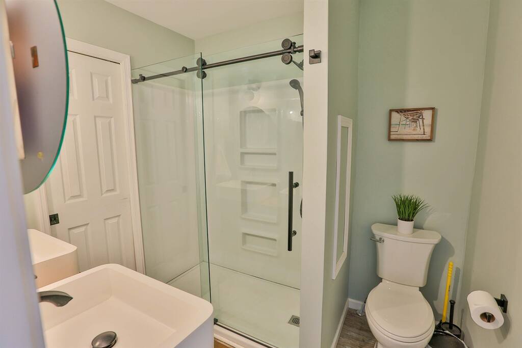 Your private bathroom features a modern glass shower, fresh green walls, and thoughtful touches like a small plant for a spa-like feel.