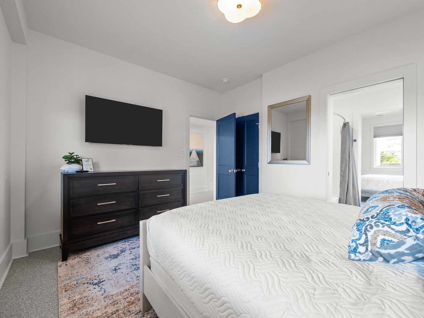 Unwind in your serene bedroom featuring a cozy queen bed, modern TV, and elegant blue accent wardrobe for all your belongings.