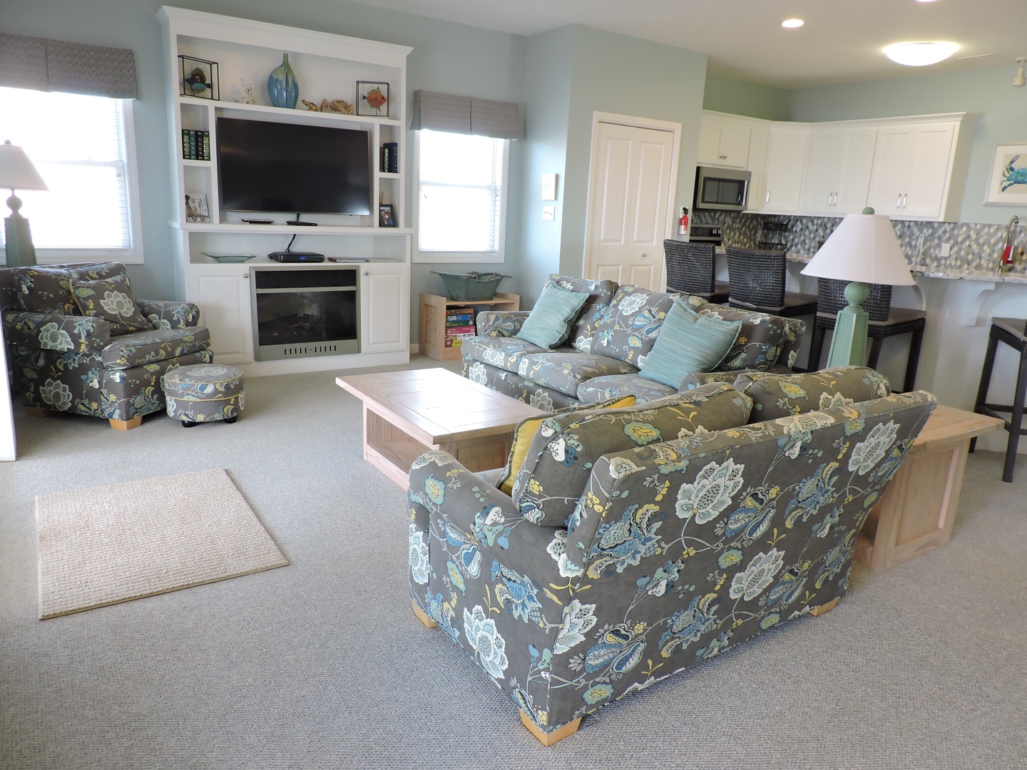 Settle into your spacious living area with plush floral seating, built-in entertainment center, and open kitchen—perfect for relaxing evenings together.