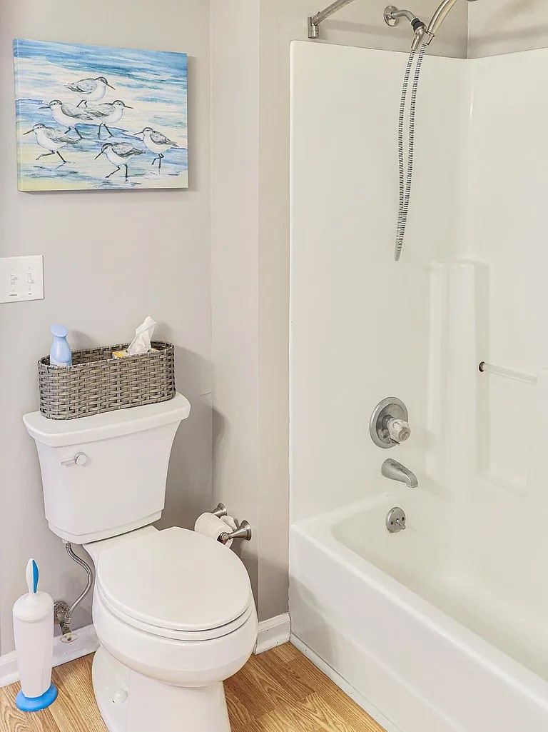 Your clean, bright bathroom features a refreshing shower-tub combo and coastal artwork that brings seaside charm to your daily routine.
