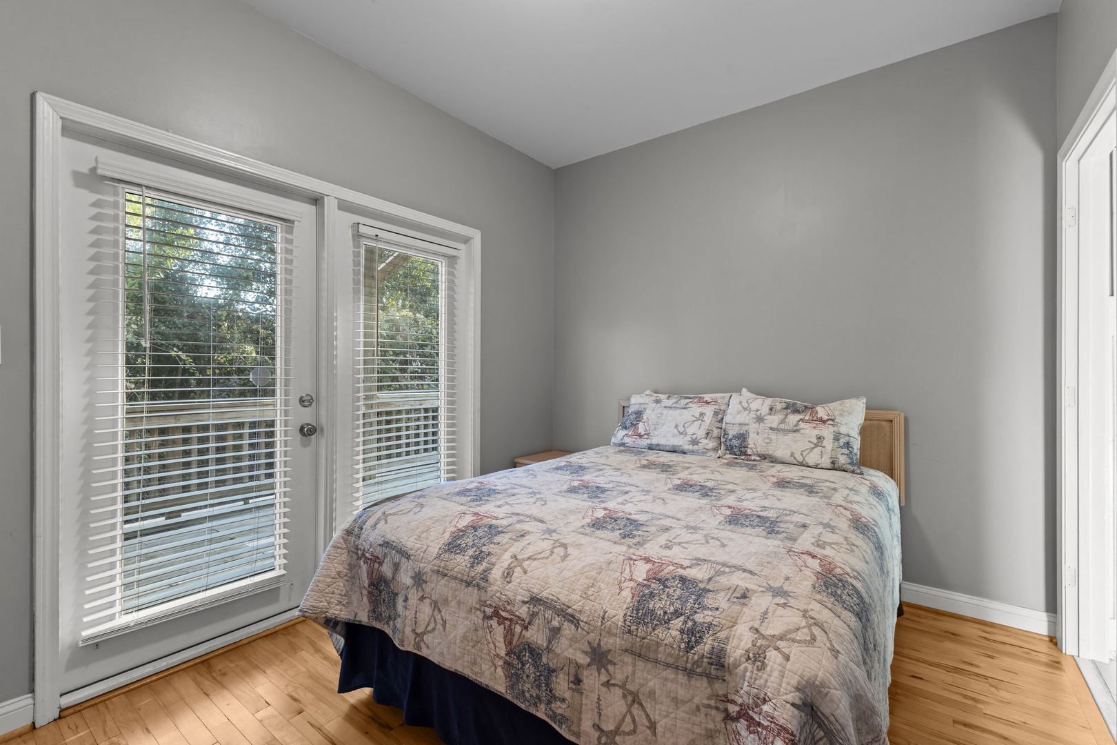 Your peaceful bedroom features soft gray walls and warm hardwood floors, with French doors opening to your private outdoor space.