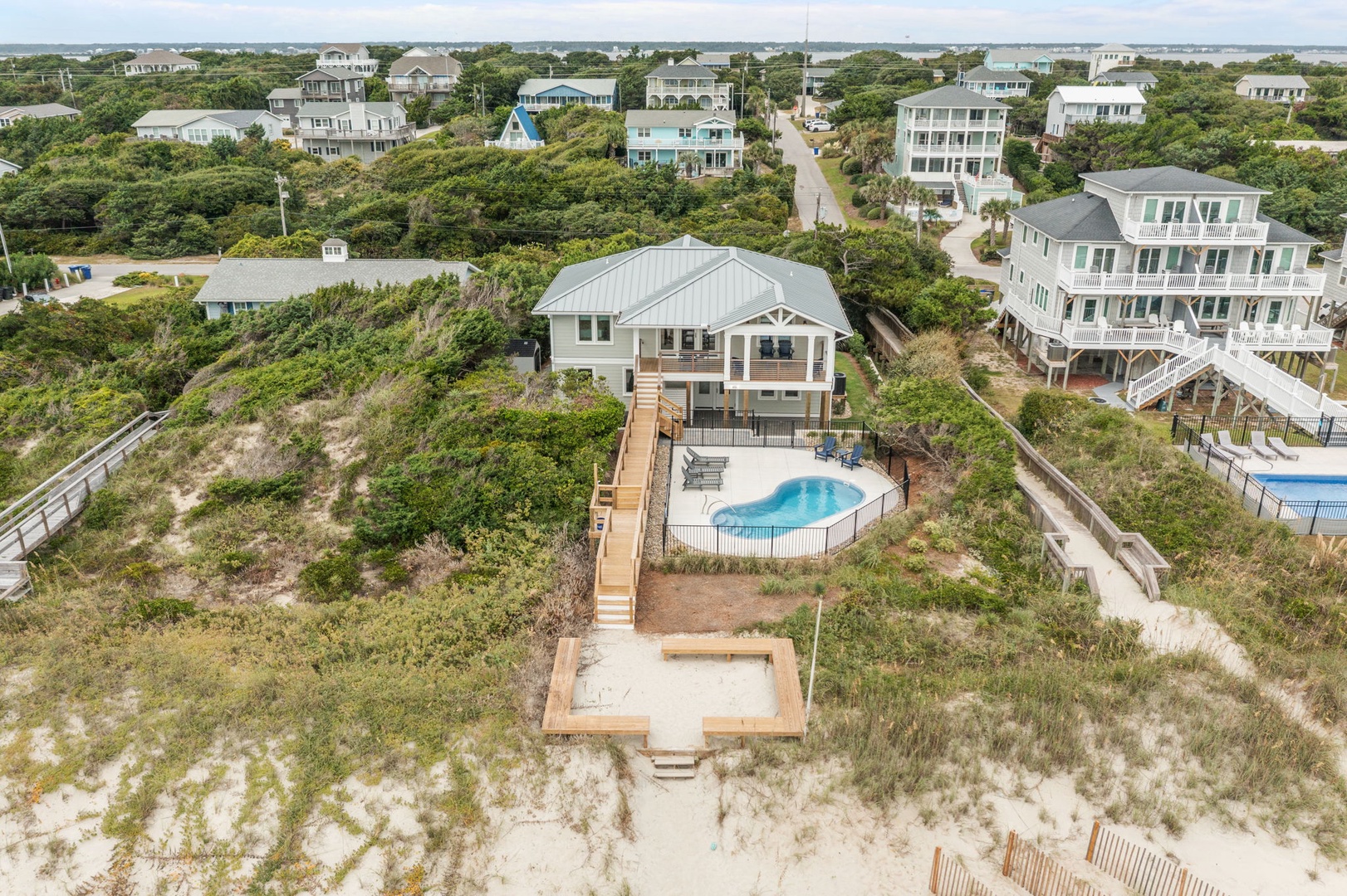Elevated beach house with private pool nestled among coastal dunes in a peaceful residential neighborhood.