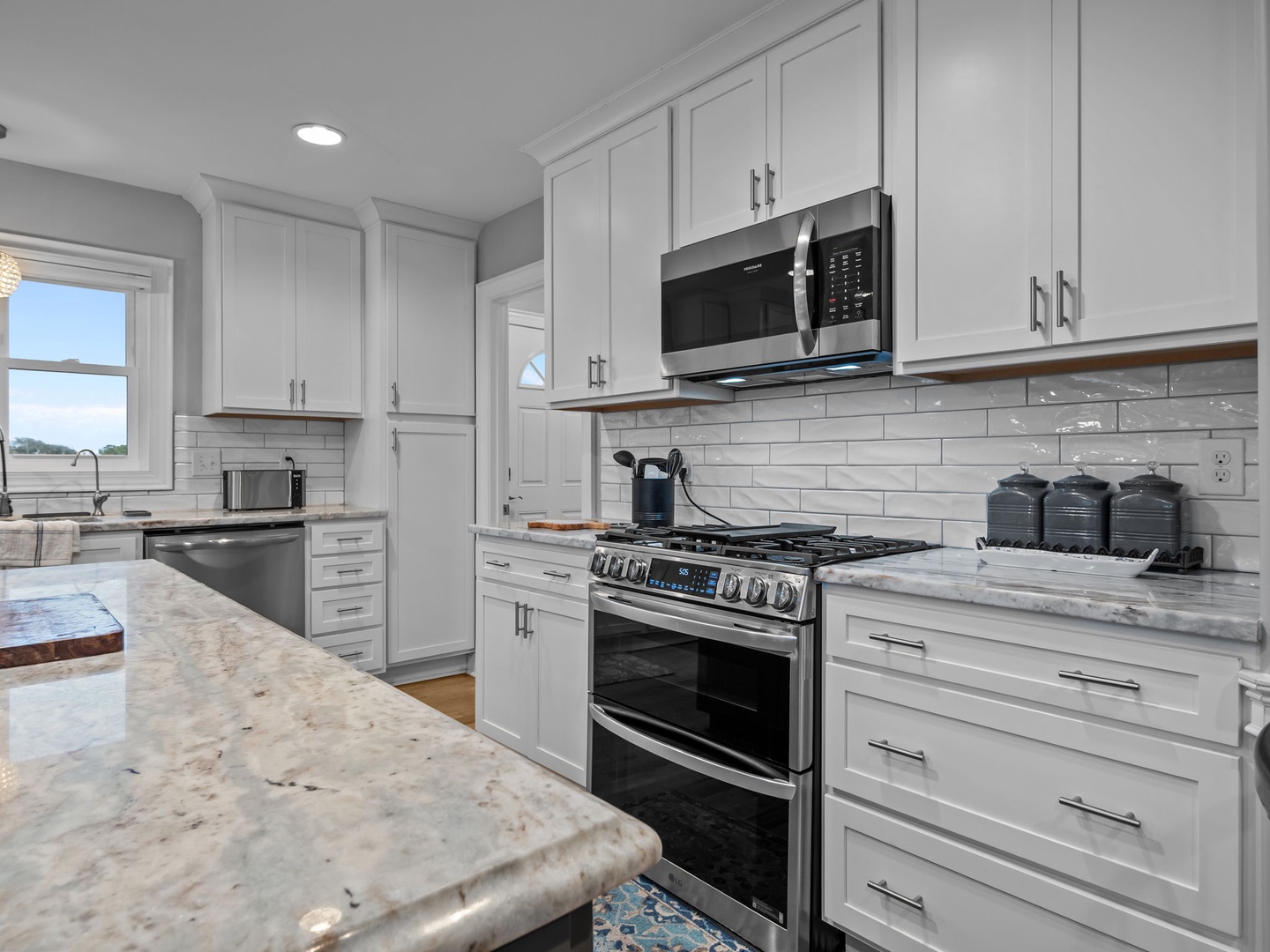 You'll love cooking in this pristine white kitchen with marble countertops, stainless steel appliances, and elegant subway tile backsplash.