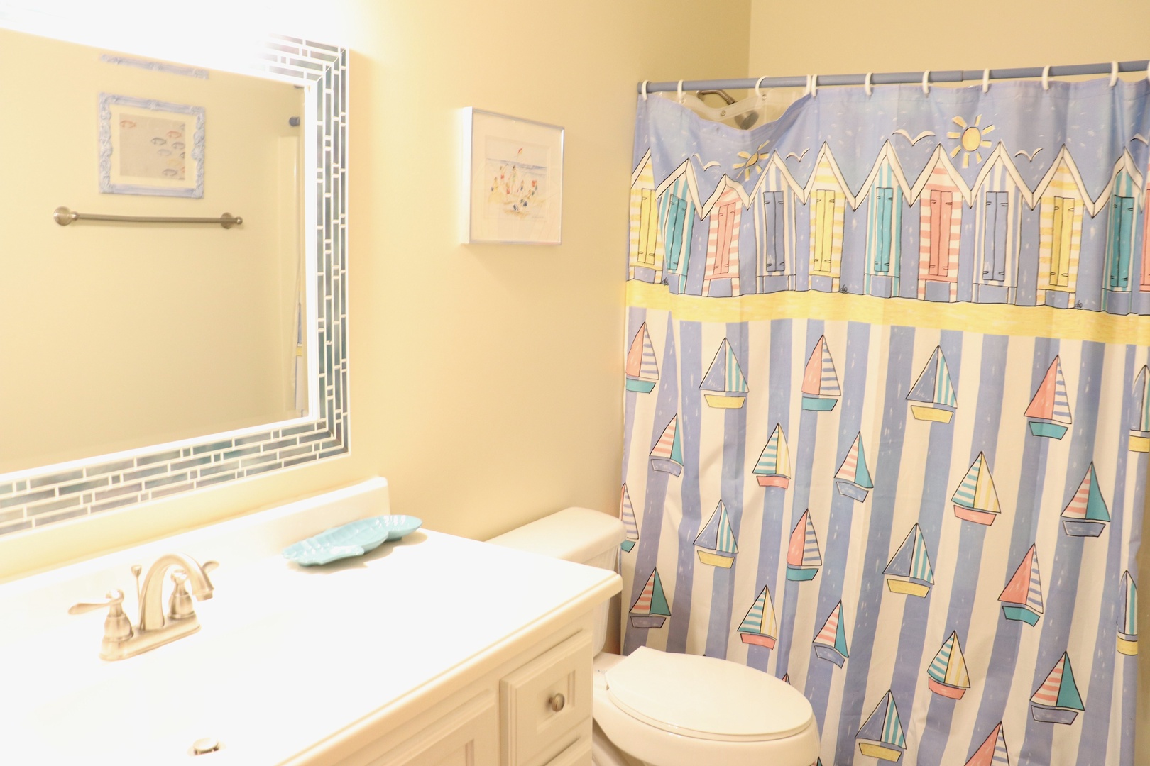 Your bright bathroom features cheerful nautical charm with colorful beach hut shower curtain and coastal artwork.
