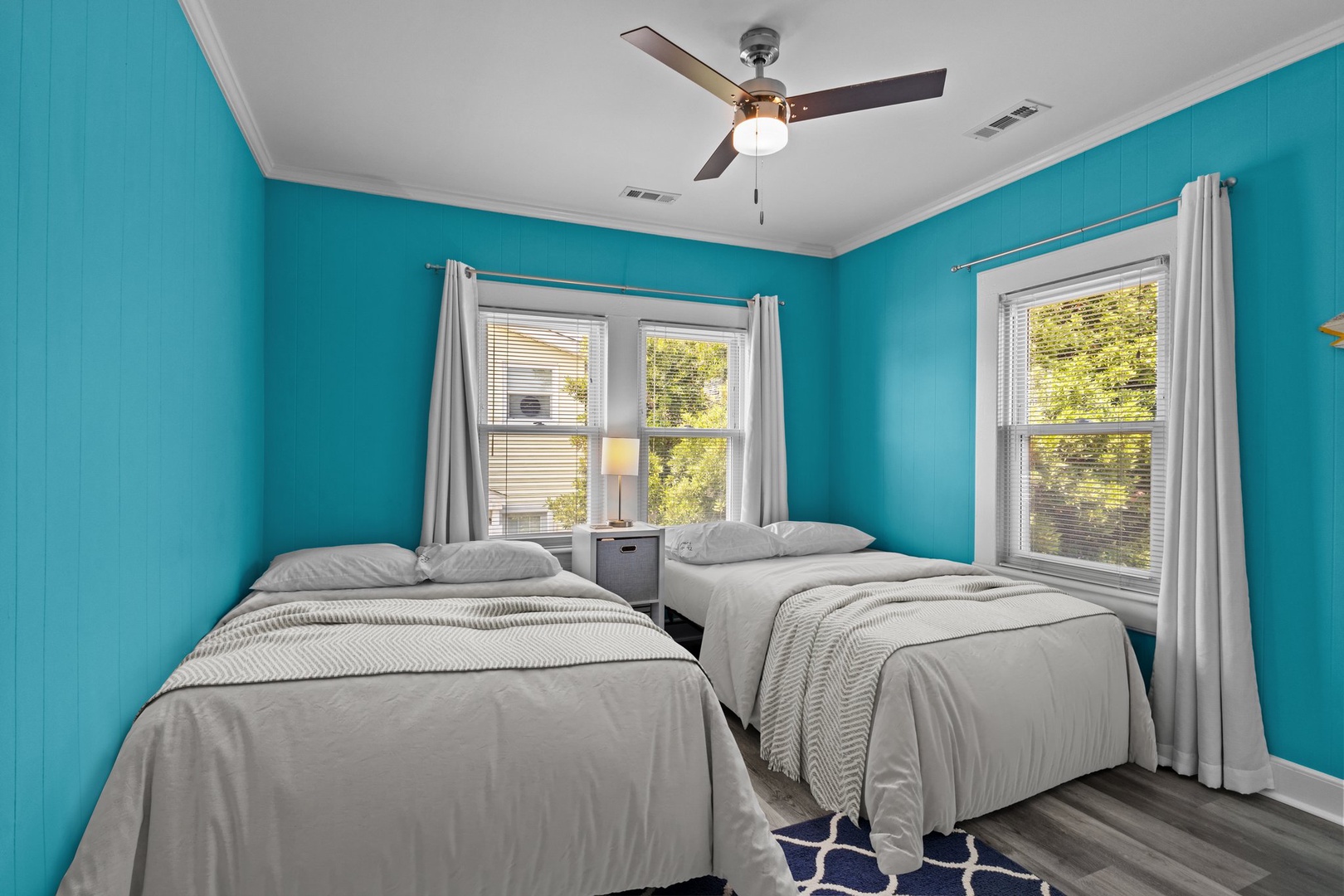 Rest peacefully in this vibrant bedroom with twin beds, cooling ceiling fan, and cheerful turquoise walls that create a refreshing coastal vibe.