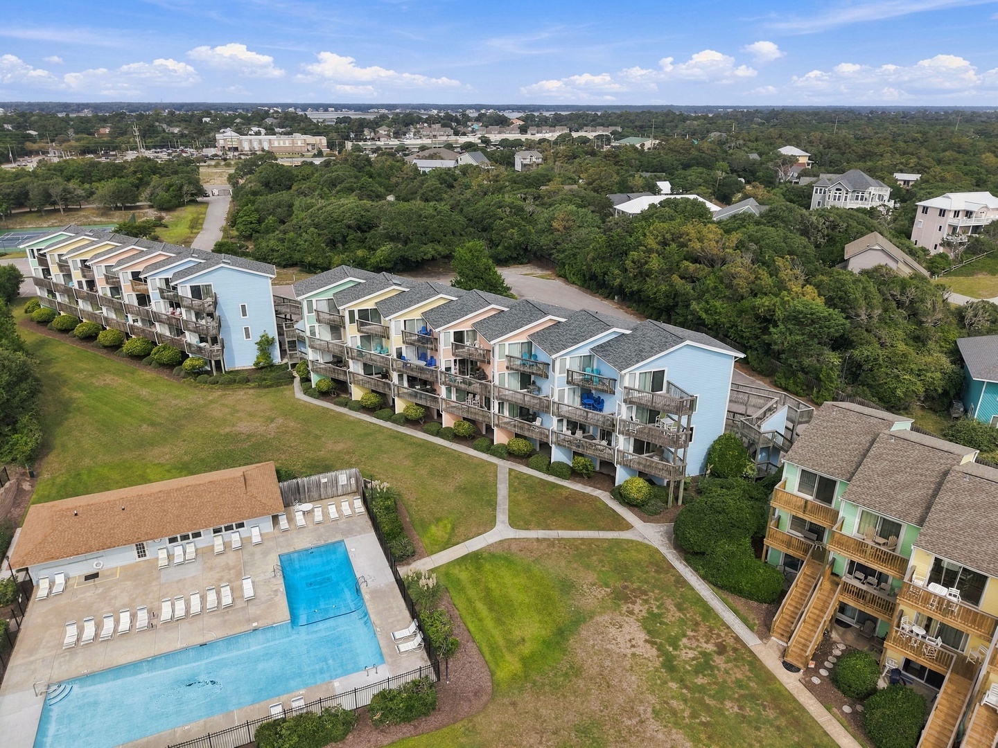 Aerial view of the vacation rental community nestled among lush trees, featuring multiple residential buildings, outdoor pools, and well-maintained grounds within a peaceful coastal neighborhood.