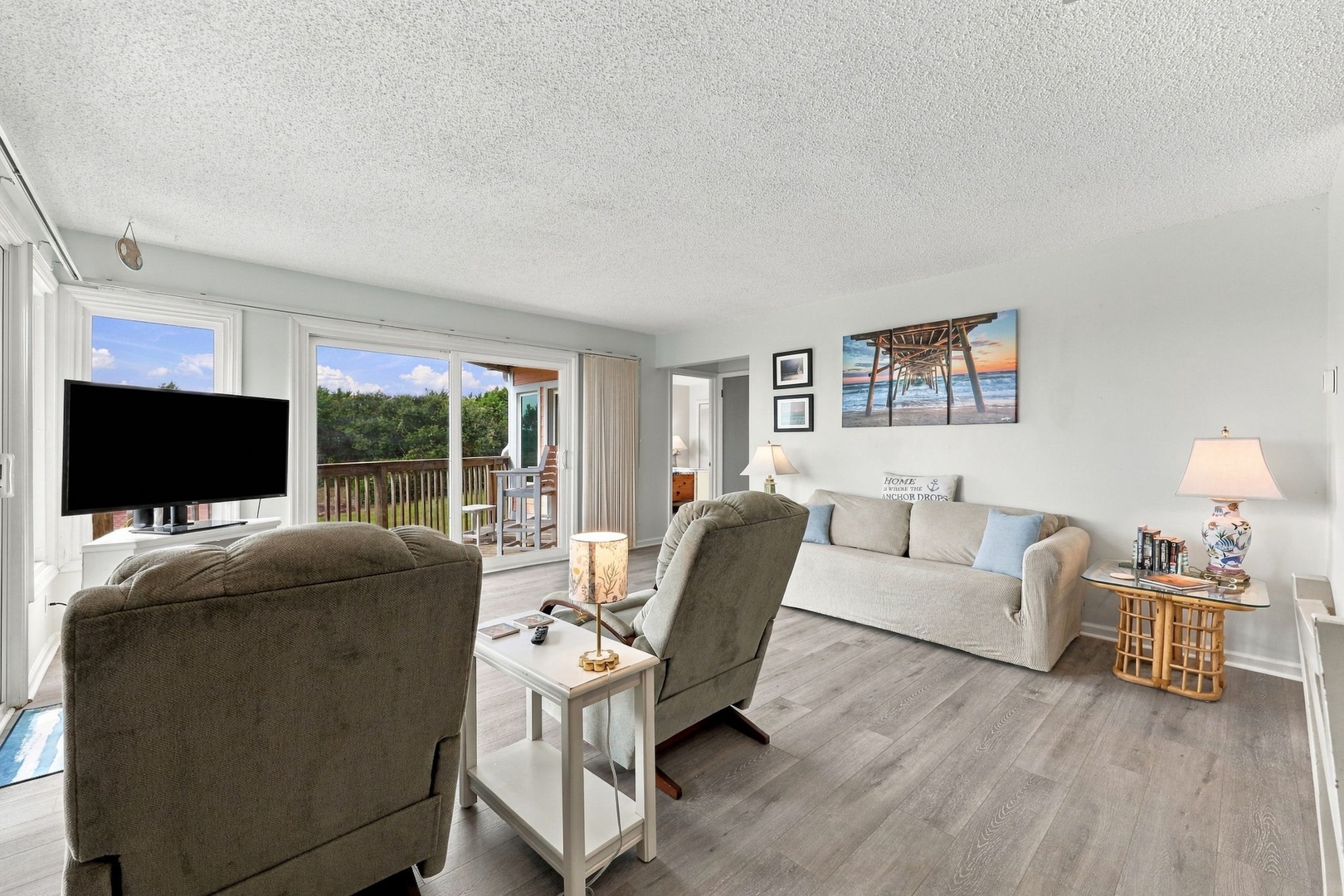 Step into your bright coastal retreat and unwind in a spacious living room designed for relaxation. Sink into plush seating, enjoy your favorite shows, and let the soft coastal light through the sliding doors set the mood for your perfect getaway.