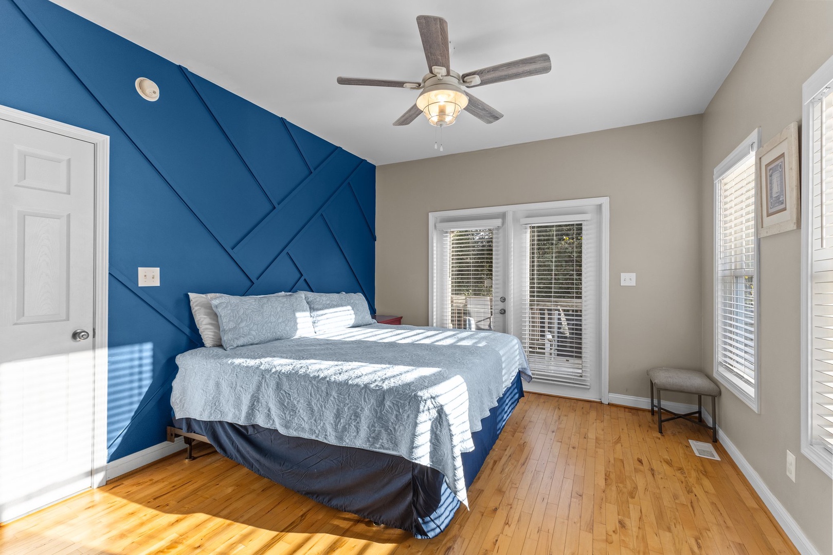 Wake up refreshed in your stylish bedroom featuring a striking blue accent wall and ceiling fan for comfort.