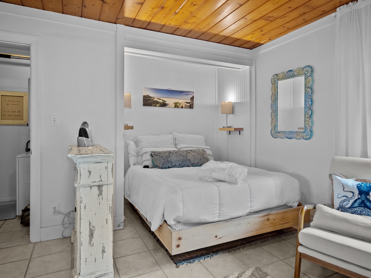 Unwind in your serene bedroom with rustic wood ceiling, crisp white linens, and charming coastal touches that create the perfect retreat.