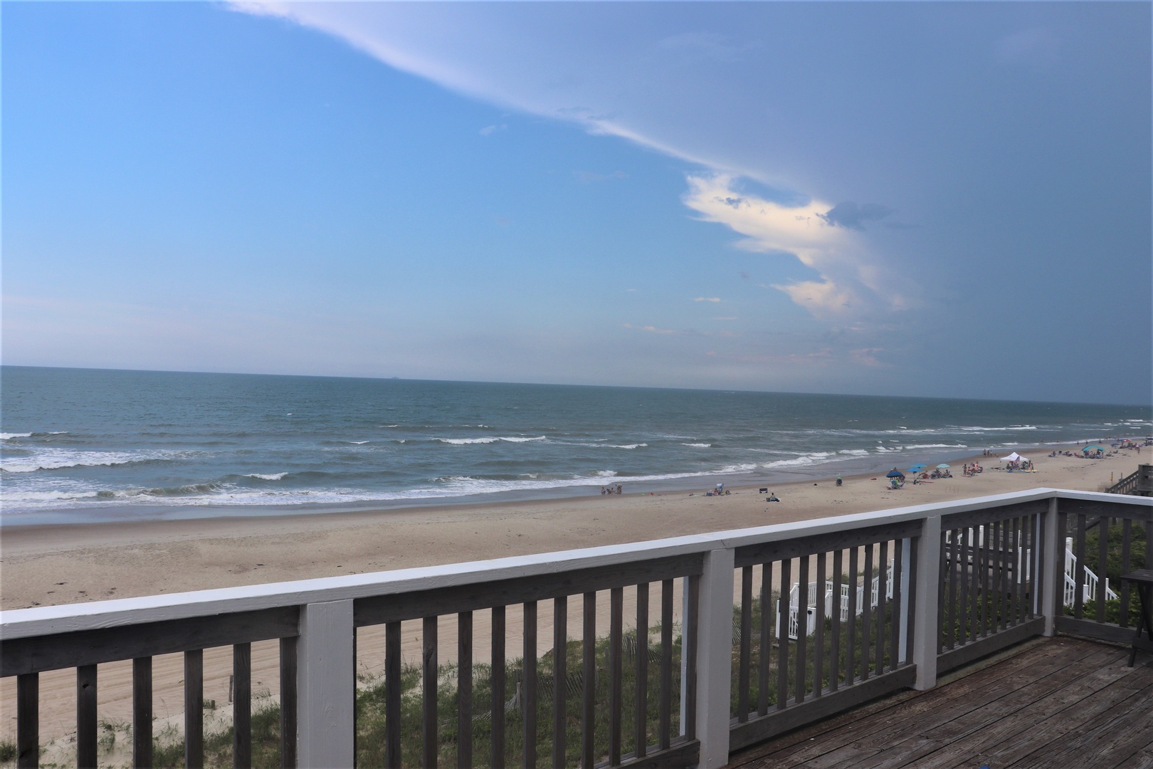 Oceanfront deck with panoramic beach views and rolling waves stretching to the horizon under expansive sky.