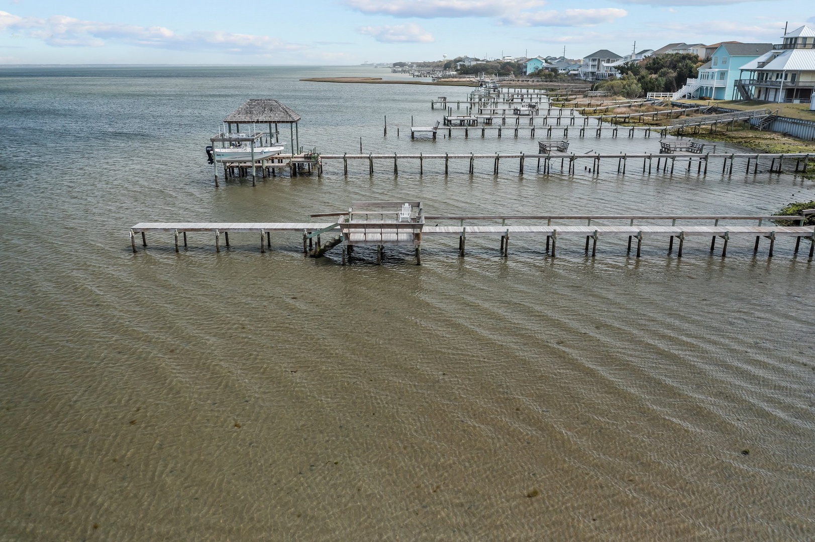 Coastal waterfront area with wooden docks extending into shallow waters, surrounded by beach houses and residential properties along the shoreline.