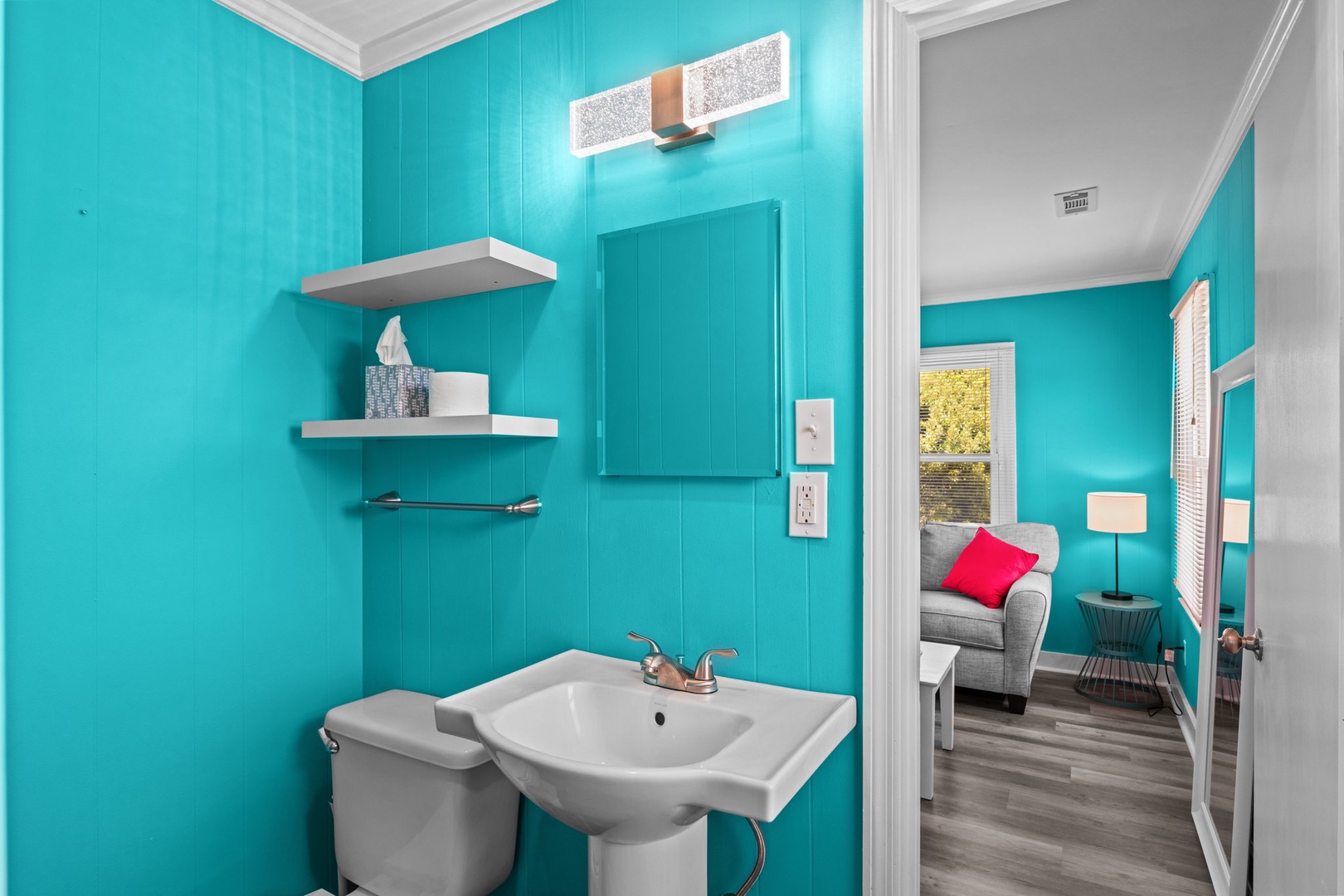 Your vibrant turquoise bathroom features thoughtful storage shelves and connects to a cozy living space with charming views.