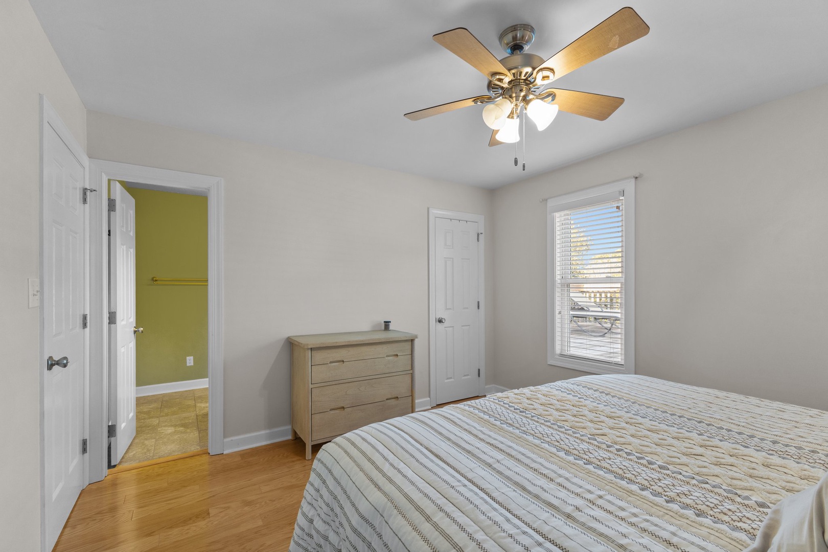 Drift off peacefully in your bright, airy bedroom with warm wood floors and gentle ceiling fan creating perfect comfort.
