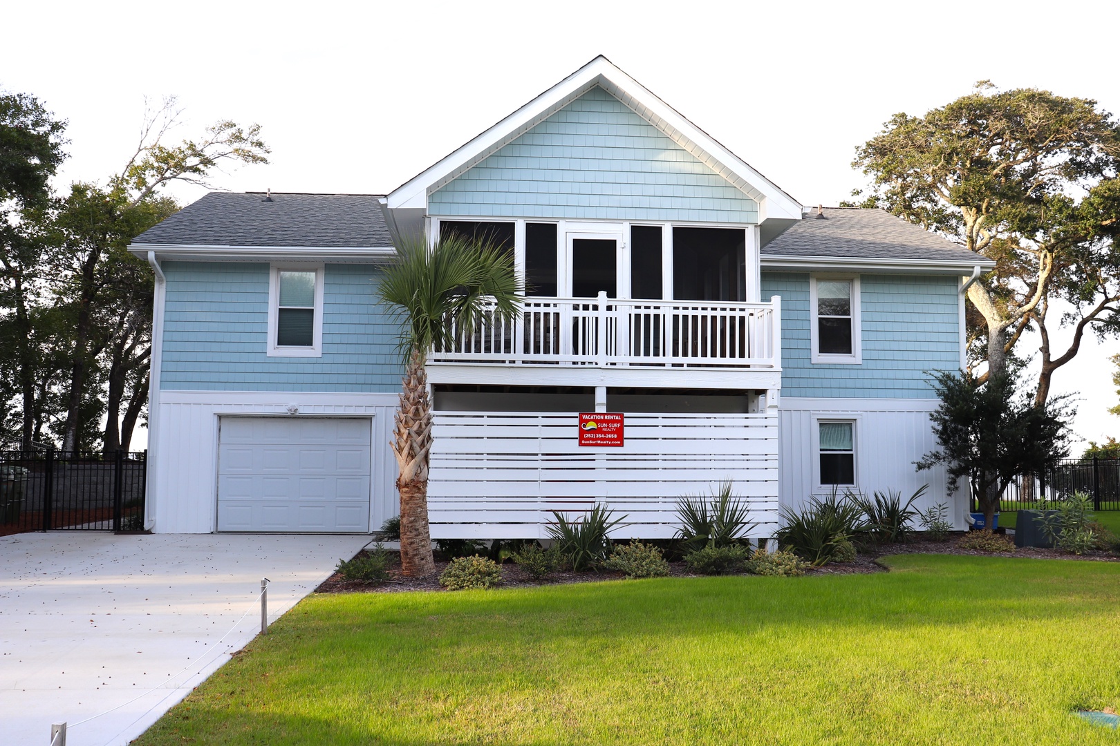 A charming coastal-style home with blue and white siding, screened porch, and tropical landscaping creates a perfect vacation retreat.