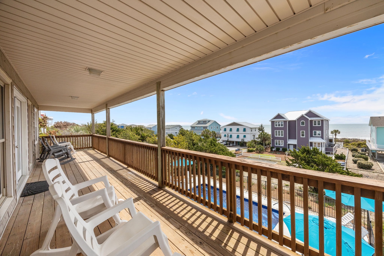 Relax on your covered deck with pool views and coastal charm under the bright blue sky.