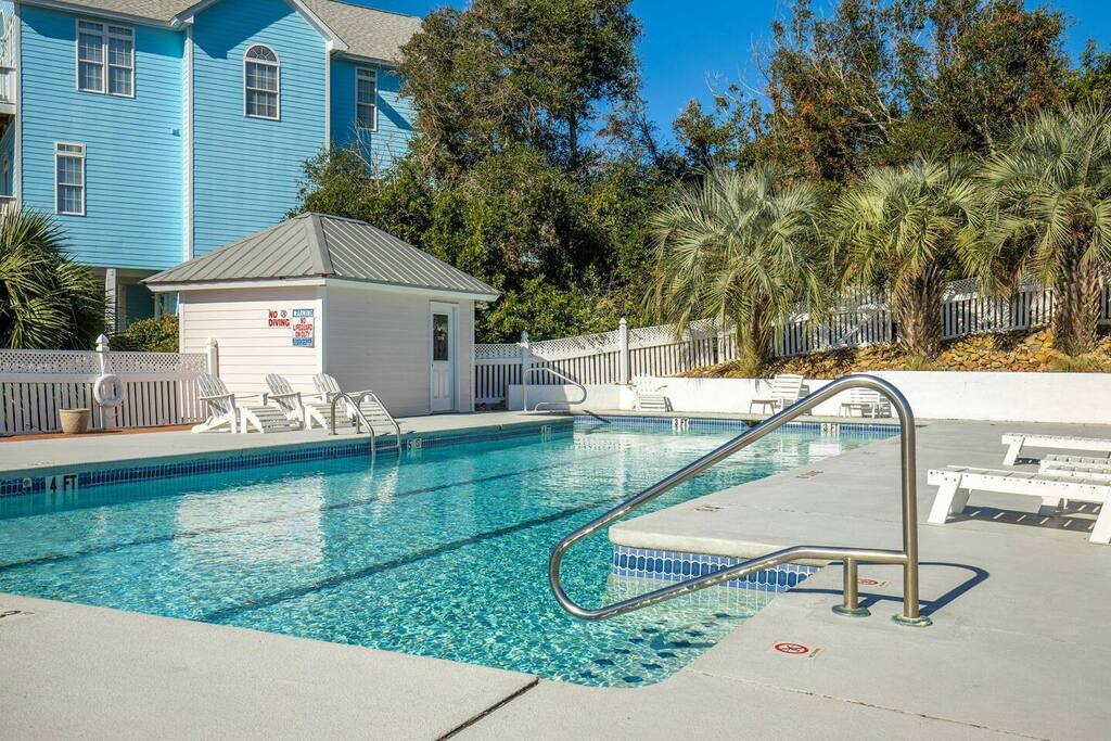 Sparkling community pool with tropical palms and lounge chairs beckons for refreshing dips under sunny skies.