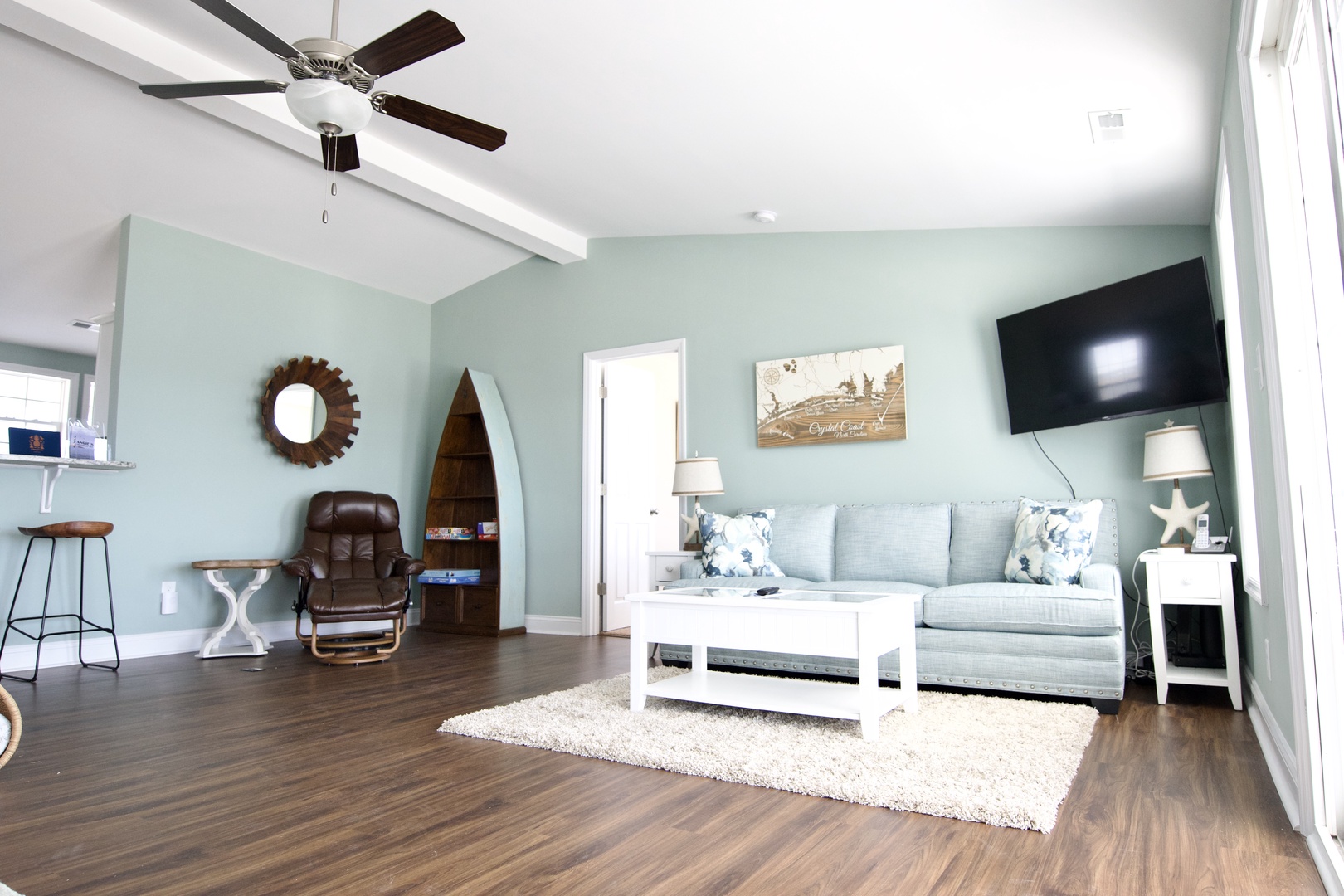 Relax in your coastal-inspired living room with soft mint walls, comfortable seating, and beach décor that makes every moment feel like vacation.