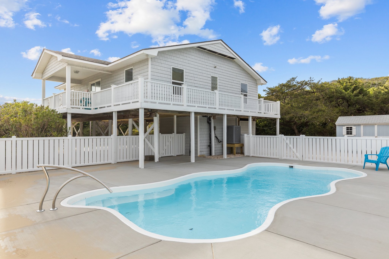Charming coastal home features an elevated design with wraparound deck and private swimming pool surrounded by natural landscaping and bright blue skies.