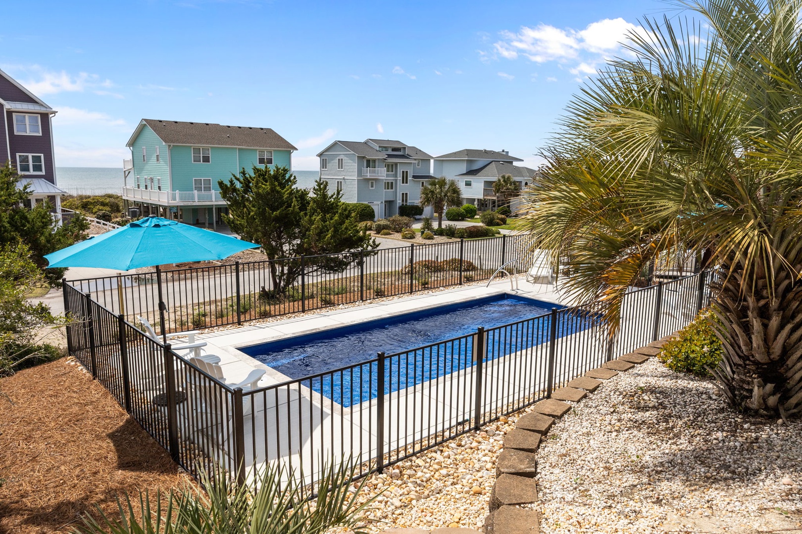 Sparkling beachside pool surrounded by tropical palms, just steps from colorful beach houses.
