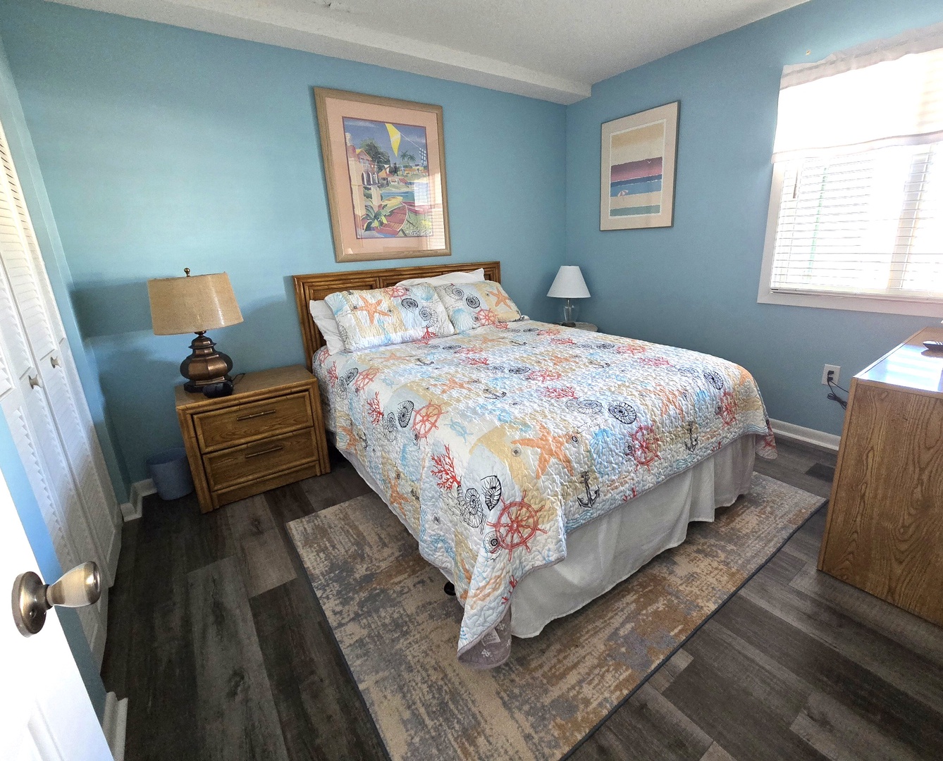 Drift off in your coastal bedroom with soothing blue walls, nautical-themed bedding, and bright natural light streaming through the windows.