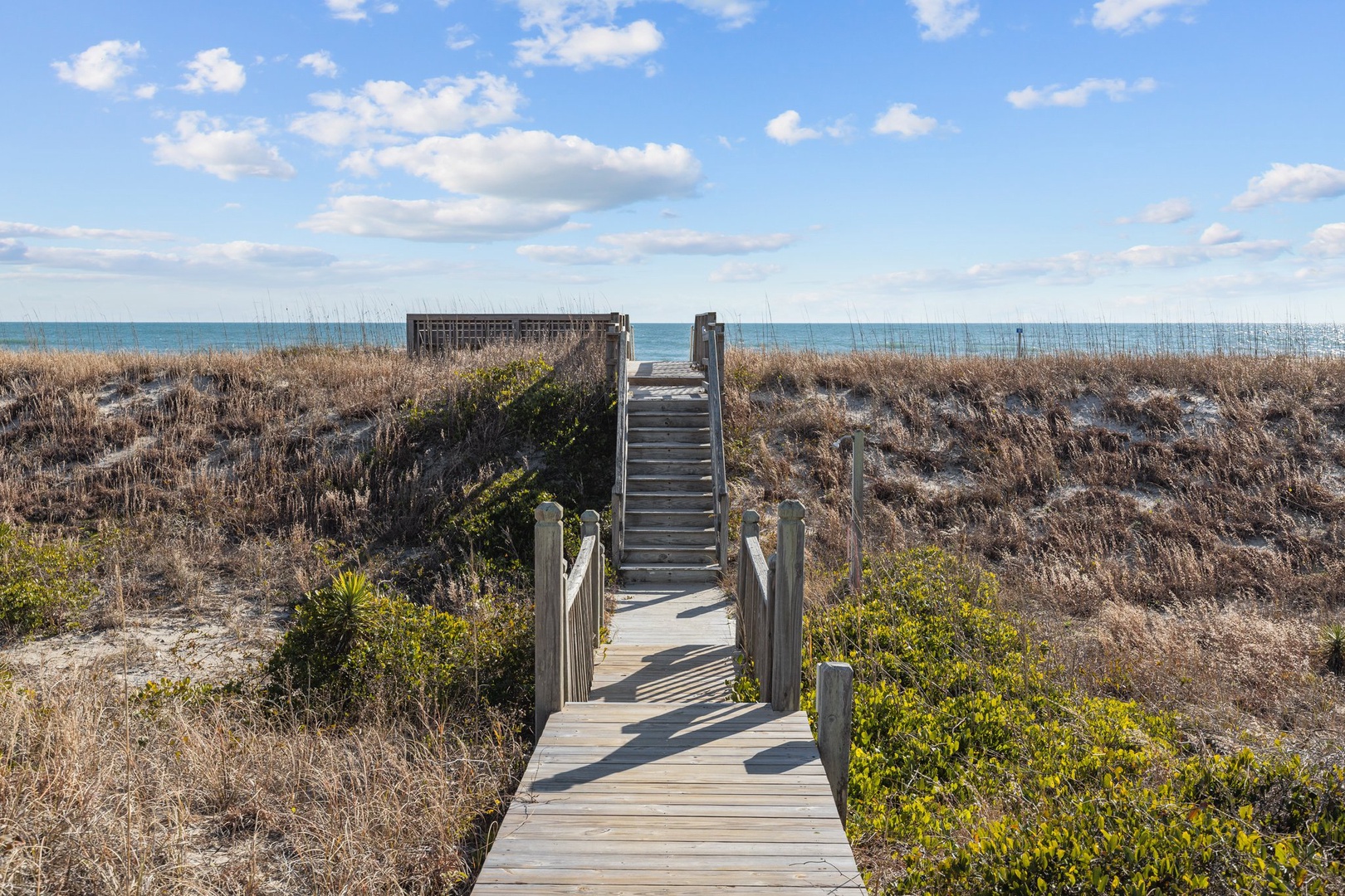 A wooden boardwalk leads through coastal dunes to the ocean, providing easy beach access from the property area.