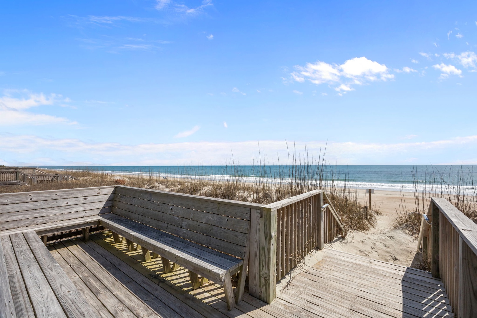 Wooden boardwalk leads to pristine white sand beach with ocean views and sea grass dunes.