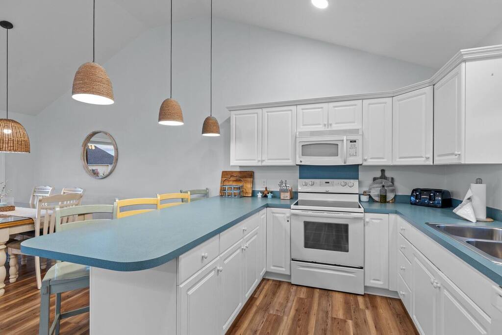 Your fully-equipped coastal kitchen features white cabinetry, blue countertops, and woven pendant lights, perfect for preparing memorable meals.
