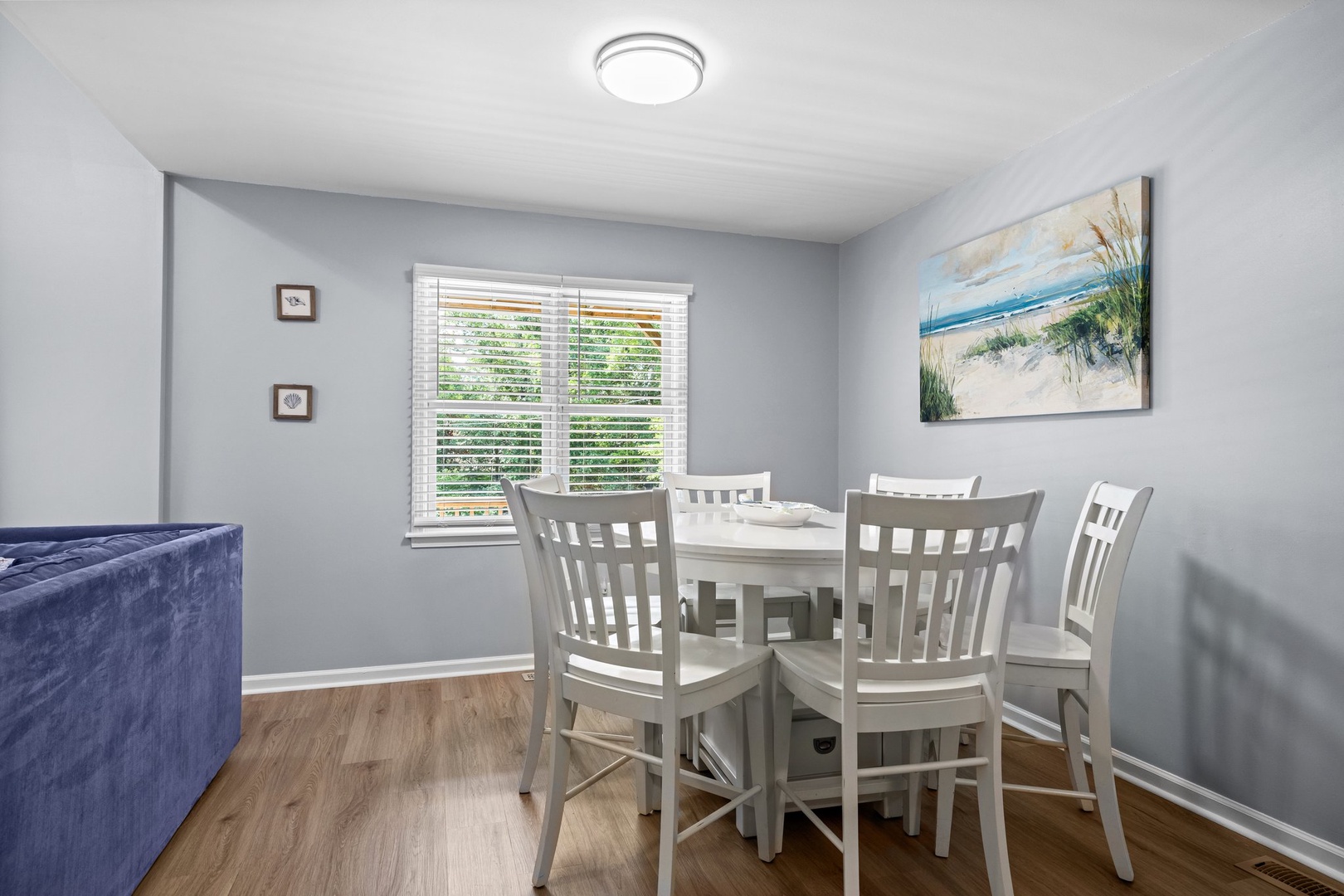 Gather around this bright dining space with coastal charm, where shared meals become cherished memories beneath peaceful beach artwork.