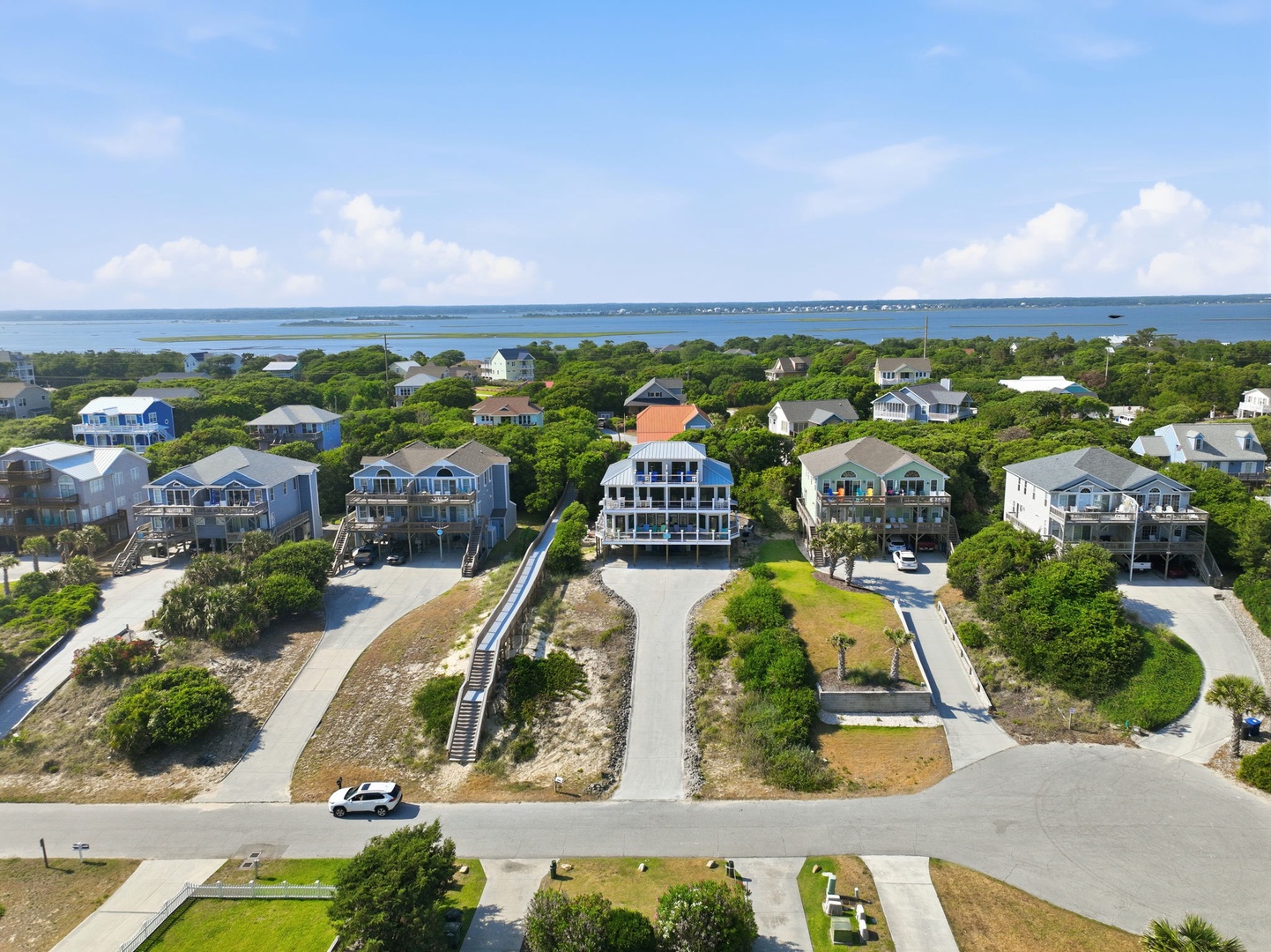 Aerial view of coastal properties nestled among lush greenery with serene bay waters in the distance and clear summer skies overhead.