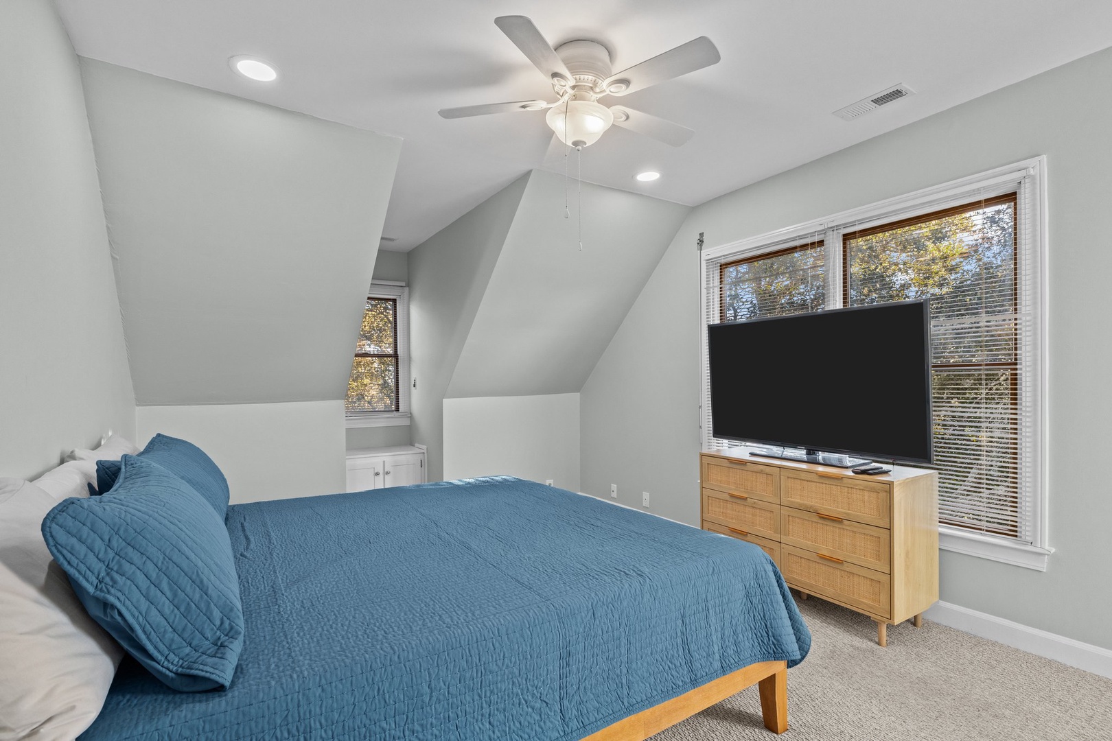 Unwind in your peaceful bedroom with cozy blue linens, modern TV entertainment, and gentle ceiling fan for perfect comfort.