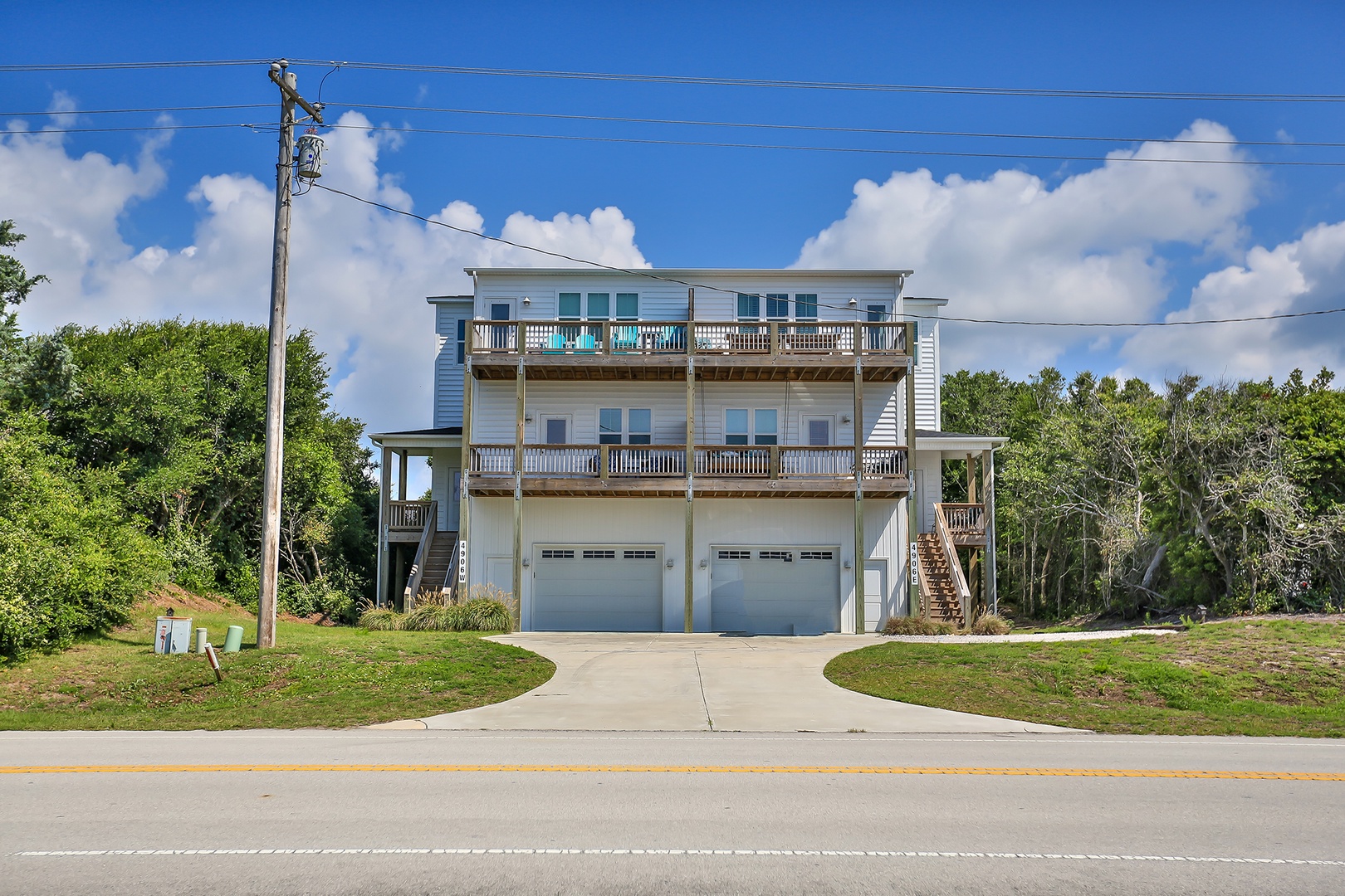 Modern beachside property with multiple balconies and parking, surrounded by lush tropical landscaping on a quiet residential street.