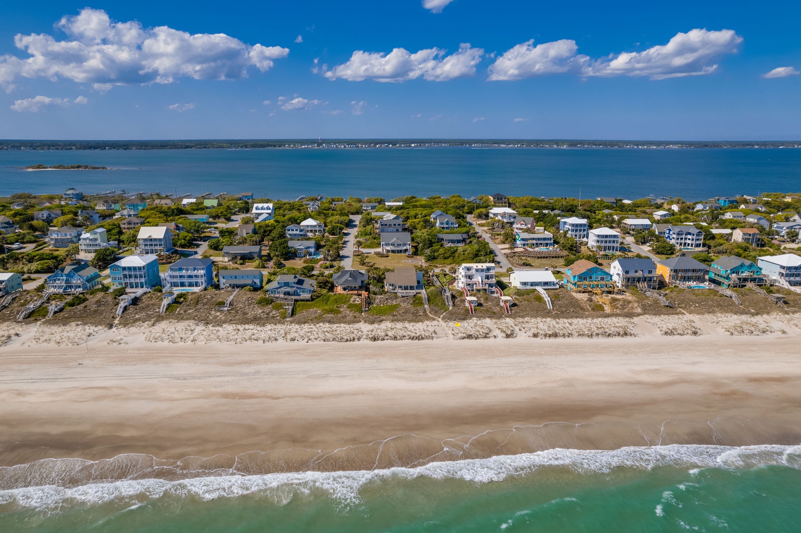 Aerial view of beachfront vacation homes along pristine coastline with turquoise waters and expansive sandy beach.