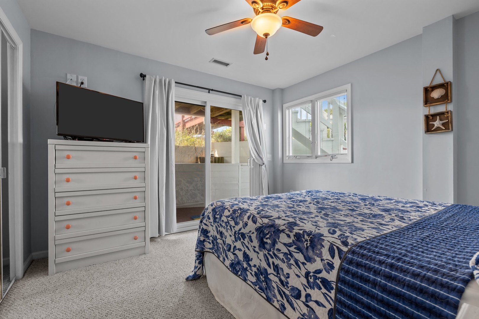 Unwind in your serene bedroom featuring coastal decor, a ceiling fan, and sliding door access to your private outdoor space.