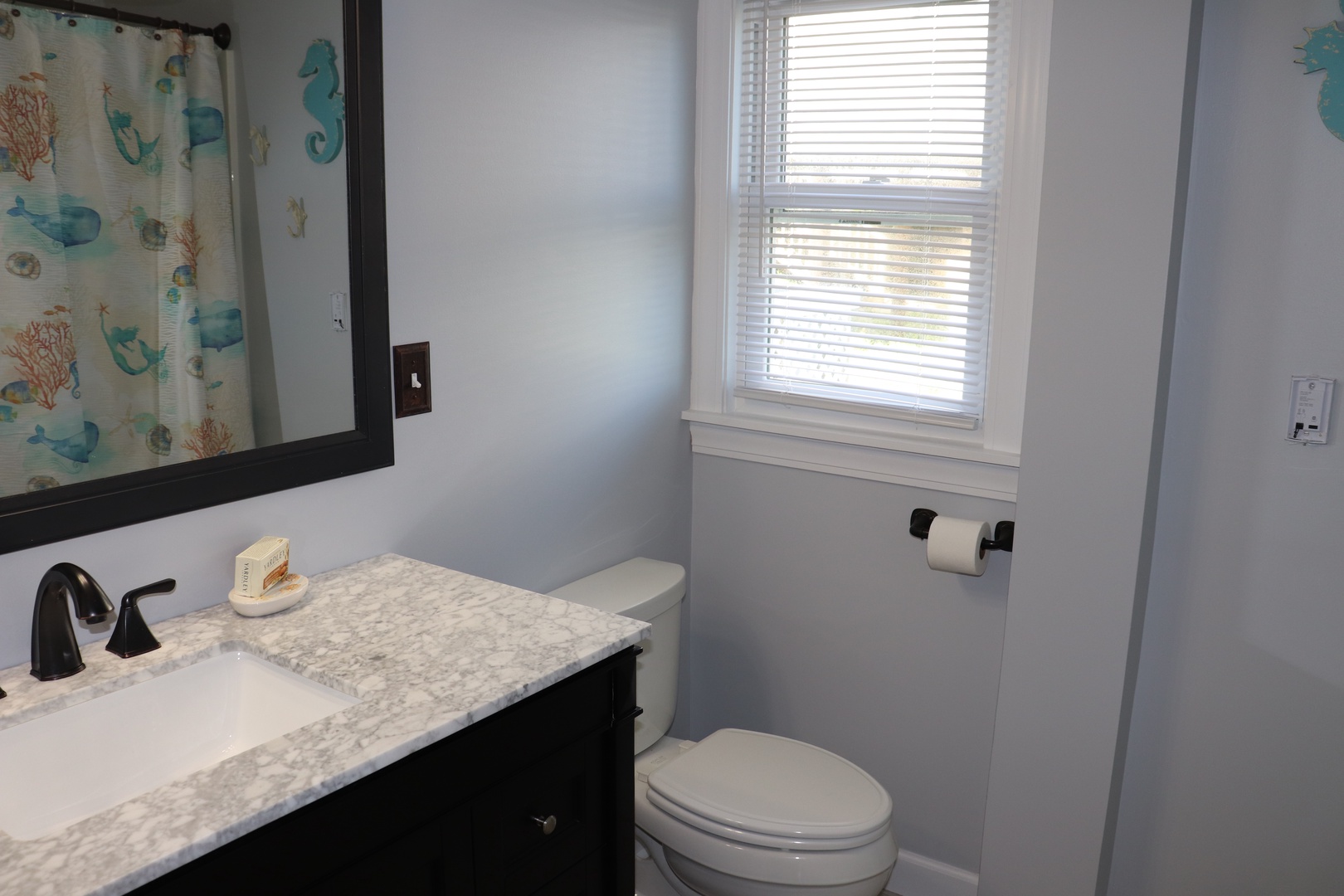 Freshen up in your bright, coastal-themed bathroom featuring granite countertops, ocean-inspired decor, and natural light from the window.